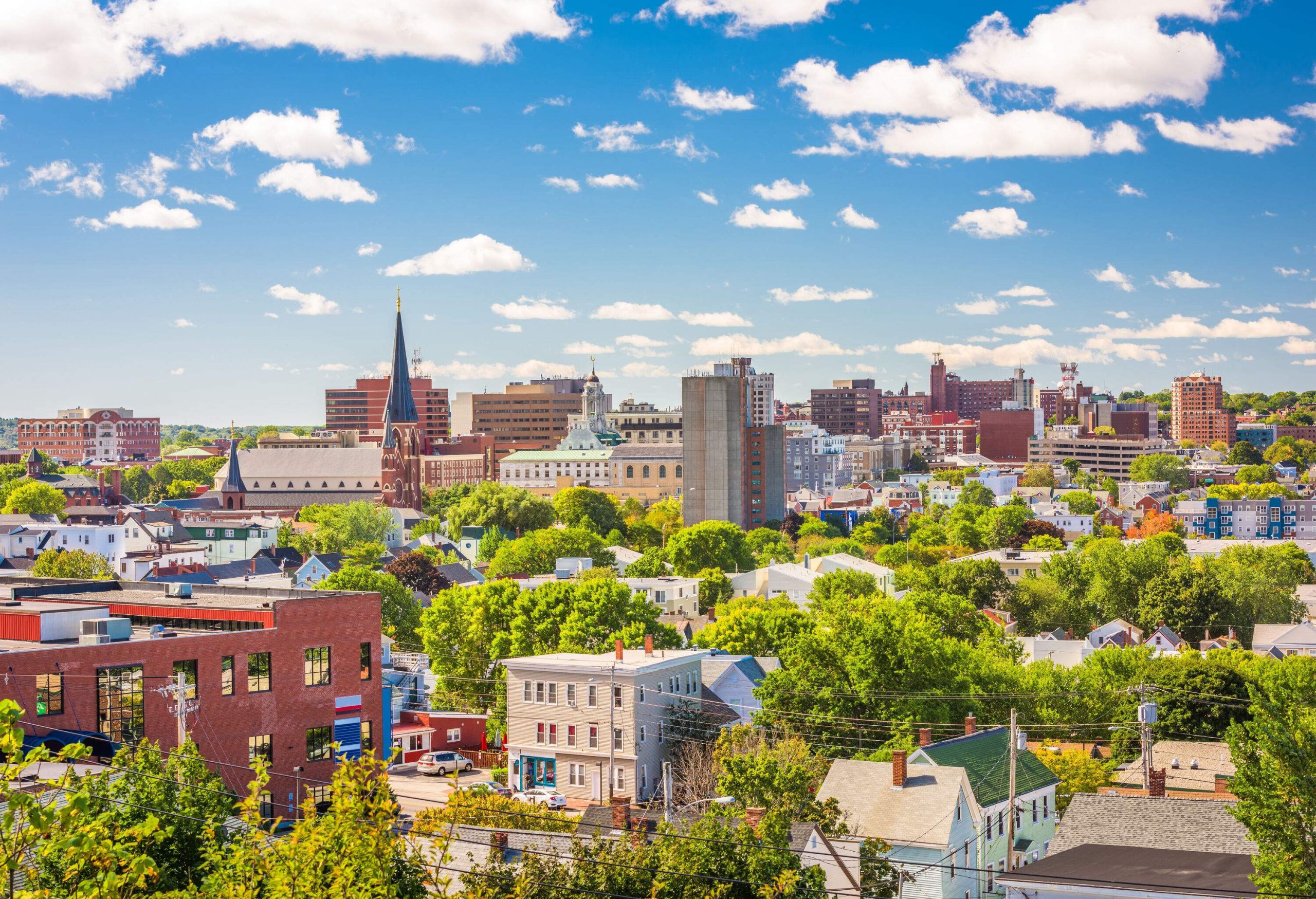 The skyline of a city is made up of tall buildings, steeples, and gable-roofed dwellings that are complemented by a beautiful sky.