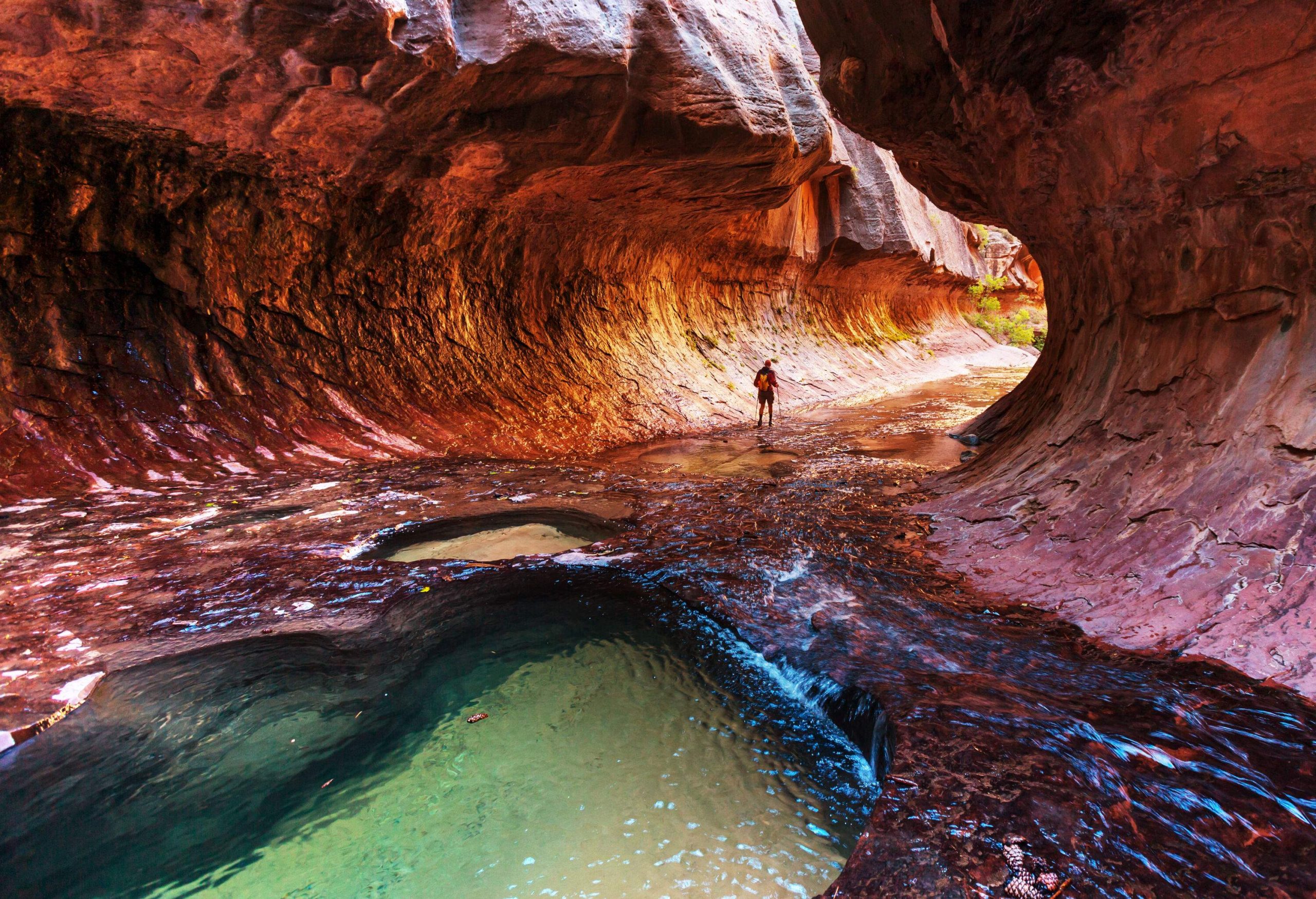 A person walking through a subway-tunnel-like narrow canyon with a swimming hole.