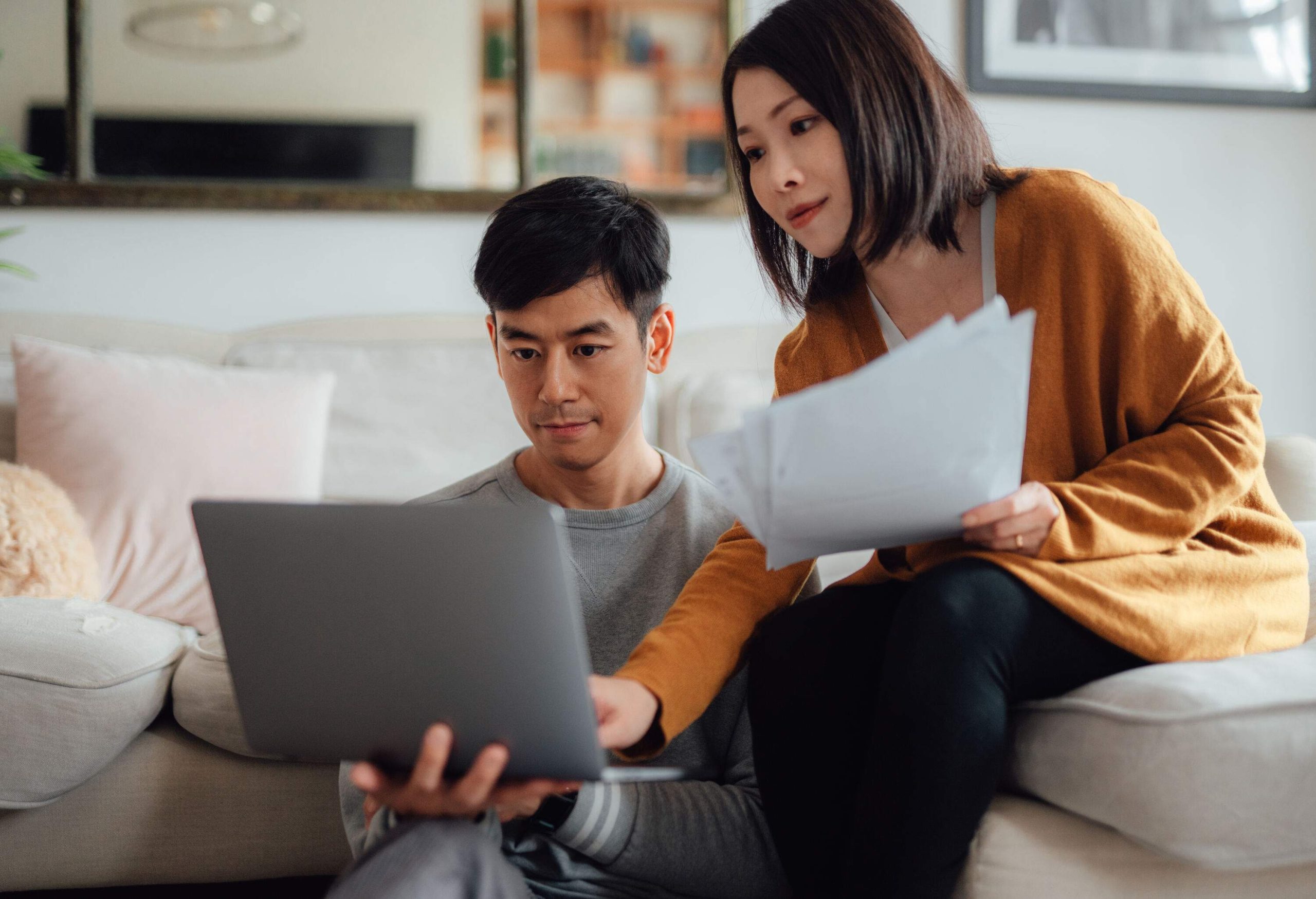 A couple sitting on a couch in the living room, working on a laptop.