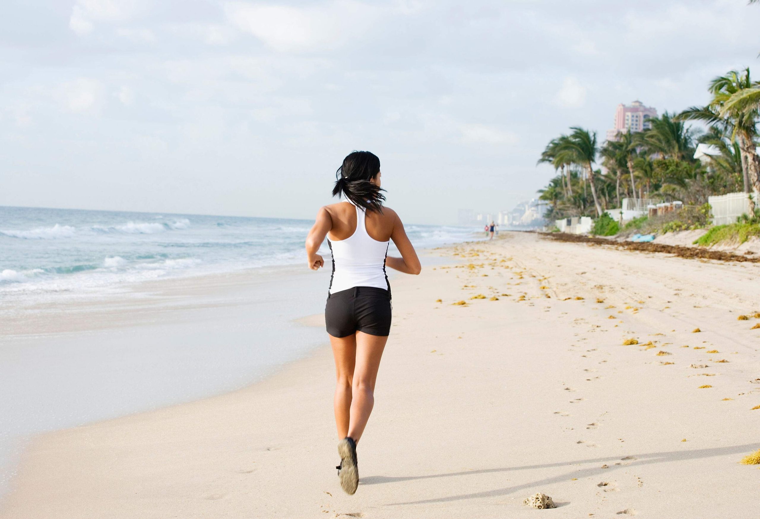 A woman in sportswear runs across a beach along a grove of palm trees.