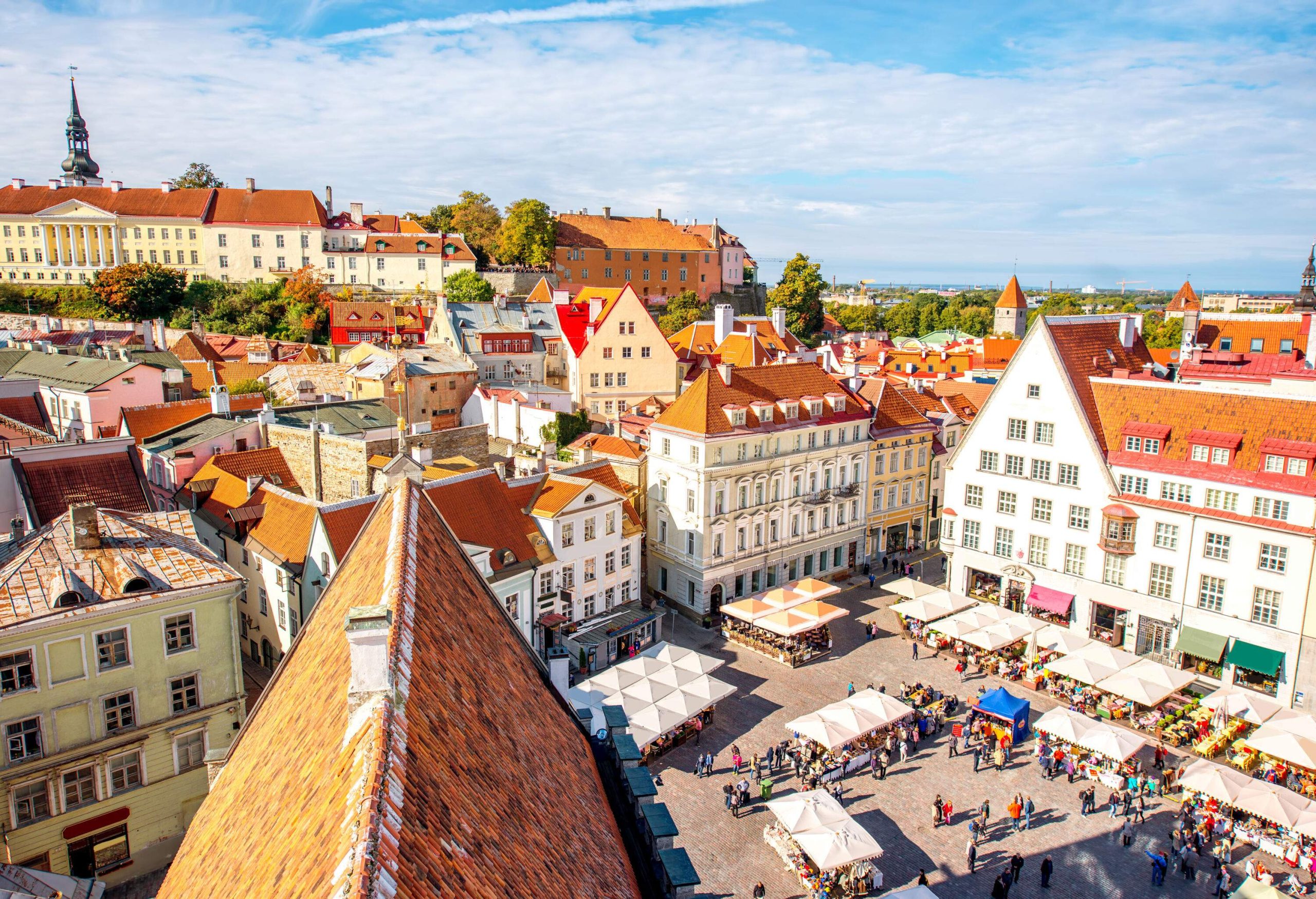 A crowded public square with vendor stalls surrounded by a cluster of buildings with red tile roofs.