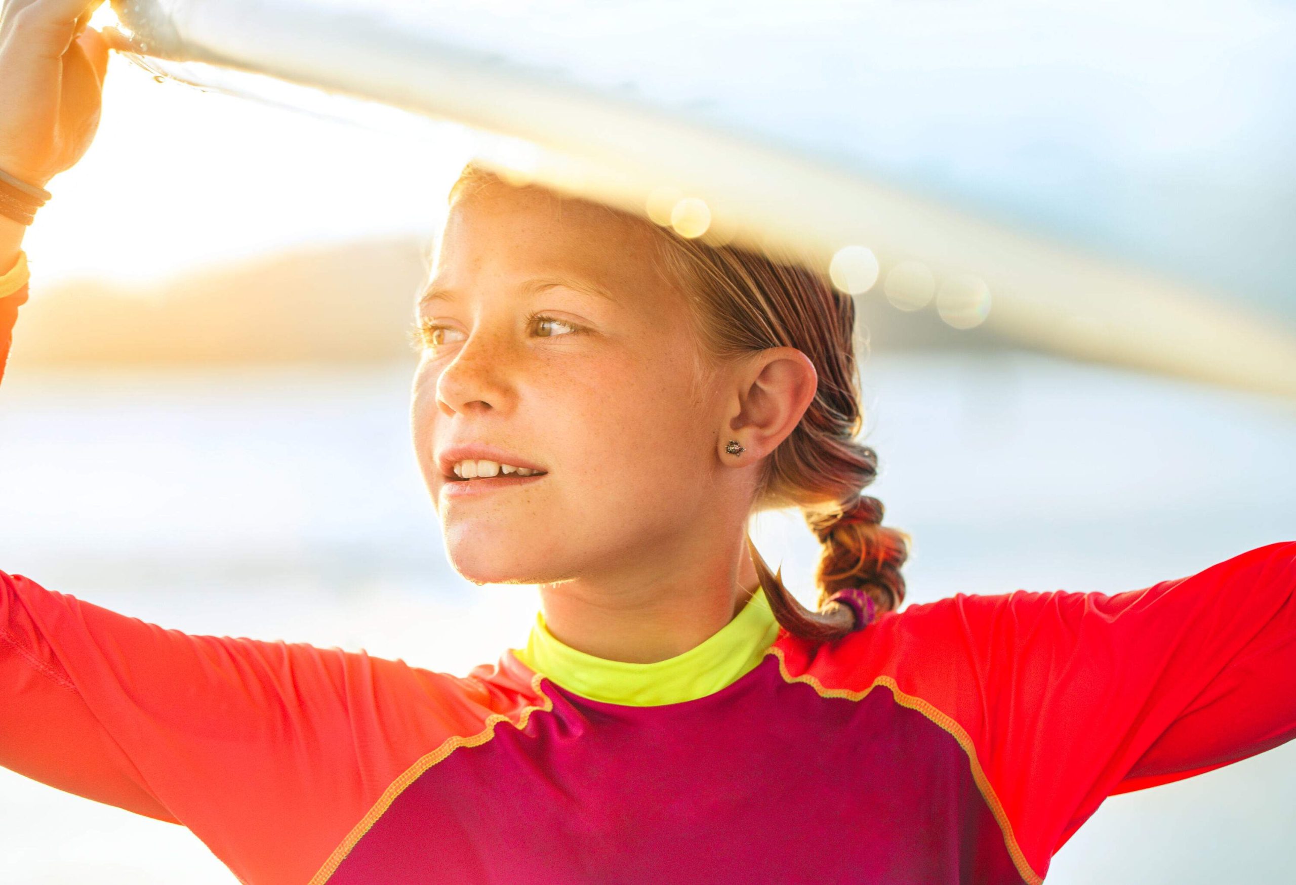 A young girl carrying a surfboard over her head.