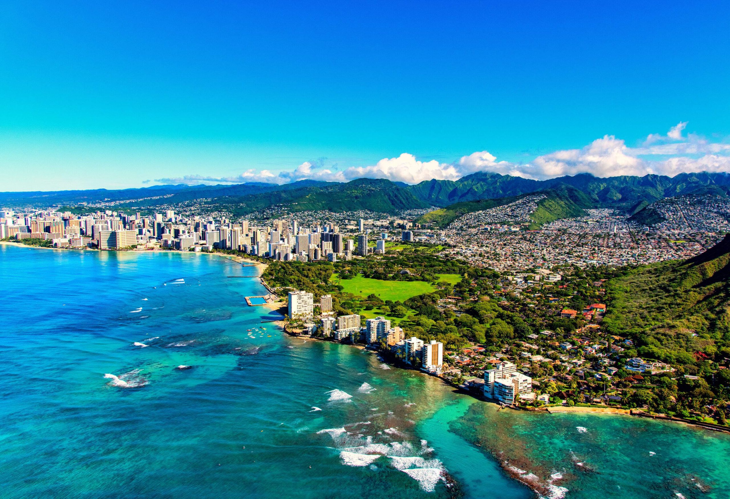 The entire coastline of Honolulu, Hawaii including the base of Diamond Head crater and state park, past the hotel lined Waikiki Beach towards downtown in the distance including the suburban neighborhoods dotting the hills surrounding the city center.