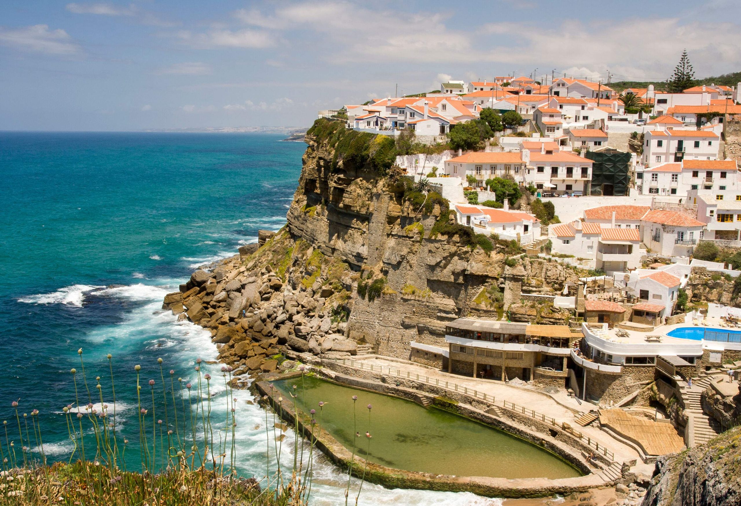 A coastal village of whitewashed buildings perched on a clifftop overlooking the blue sea.
