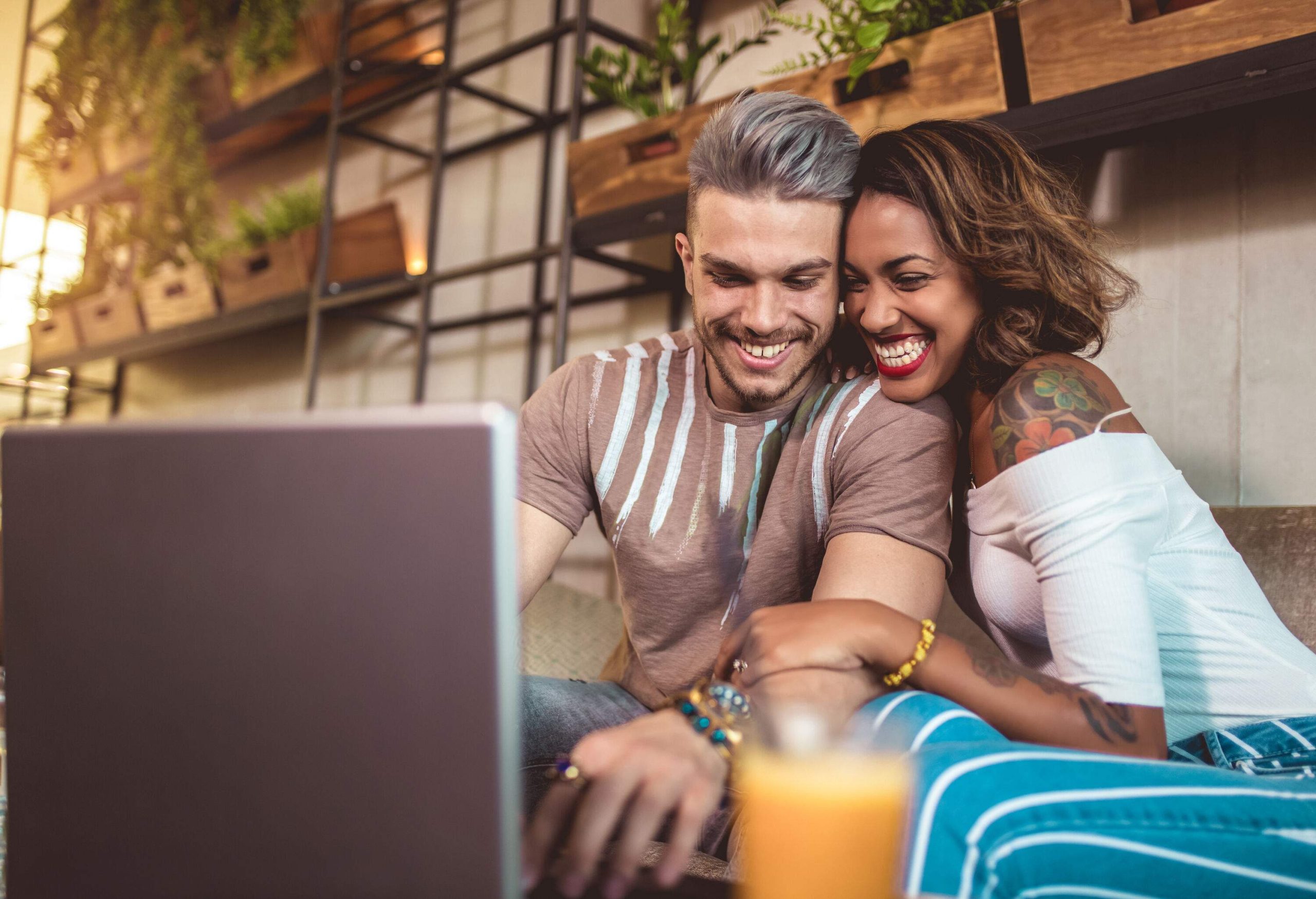 A happy couple hugs as they spend time in a cafe with a laptop in front of them.