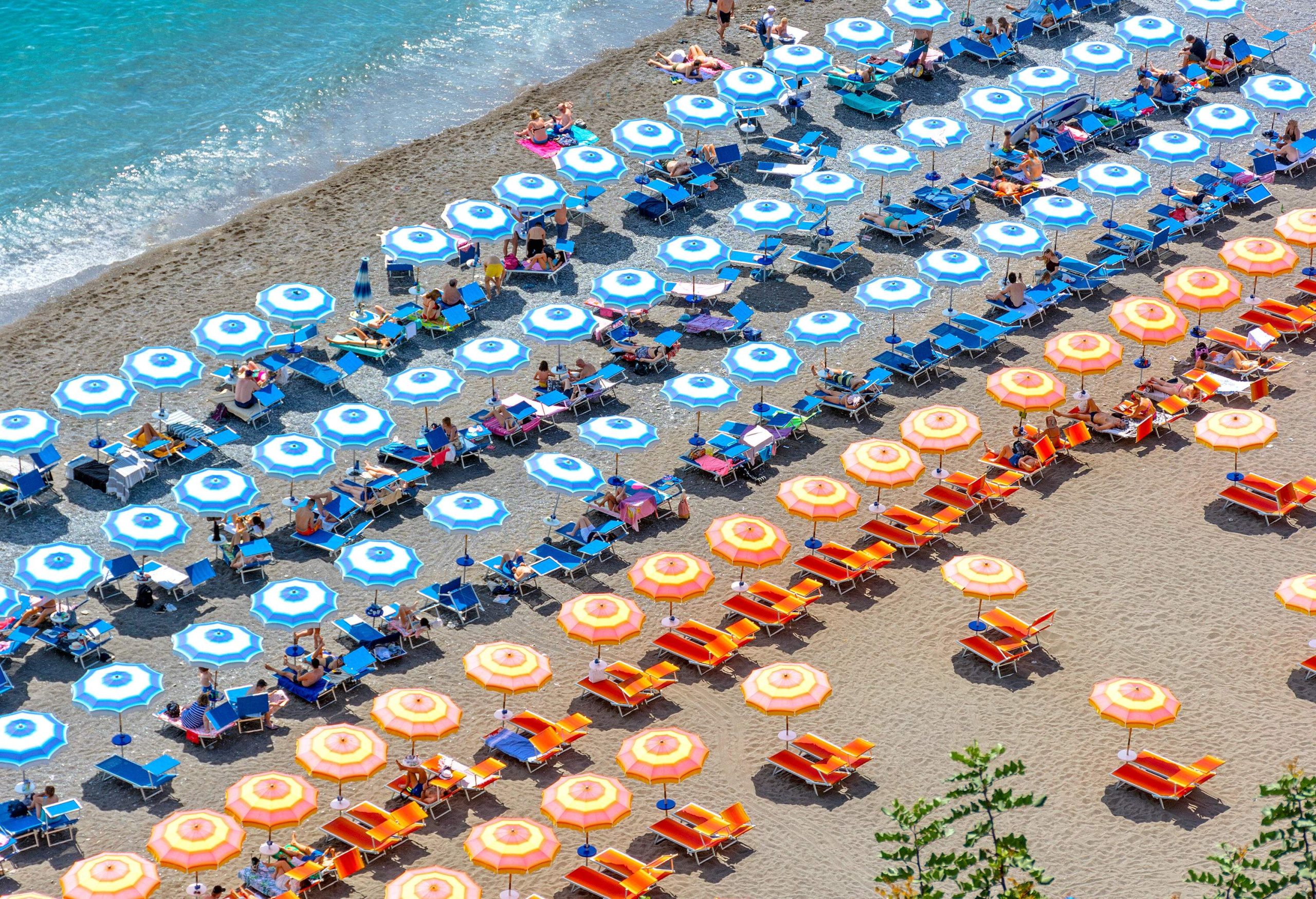 A sandy beach lined with umbrellas and loungers in blue and orange.