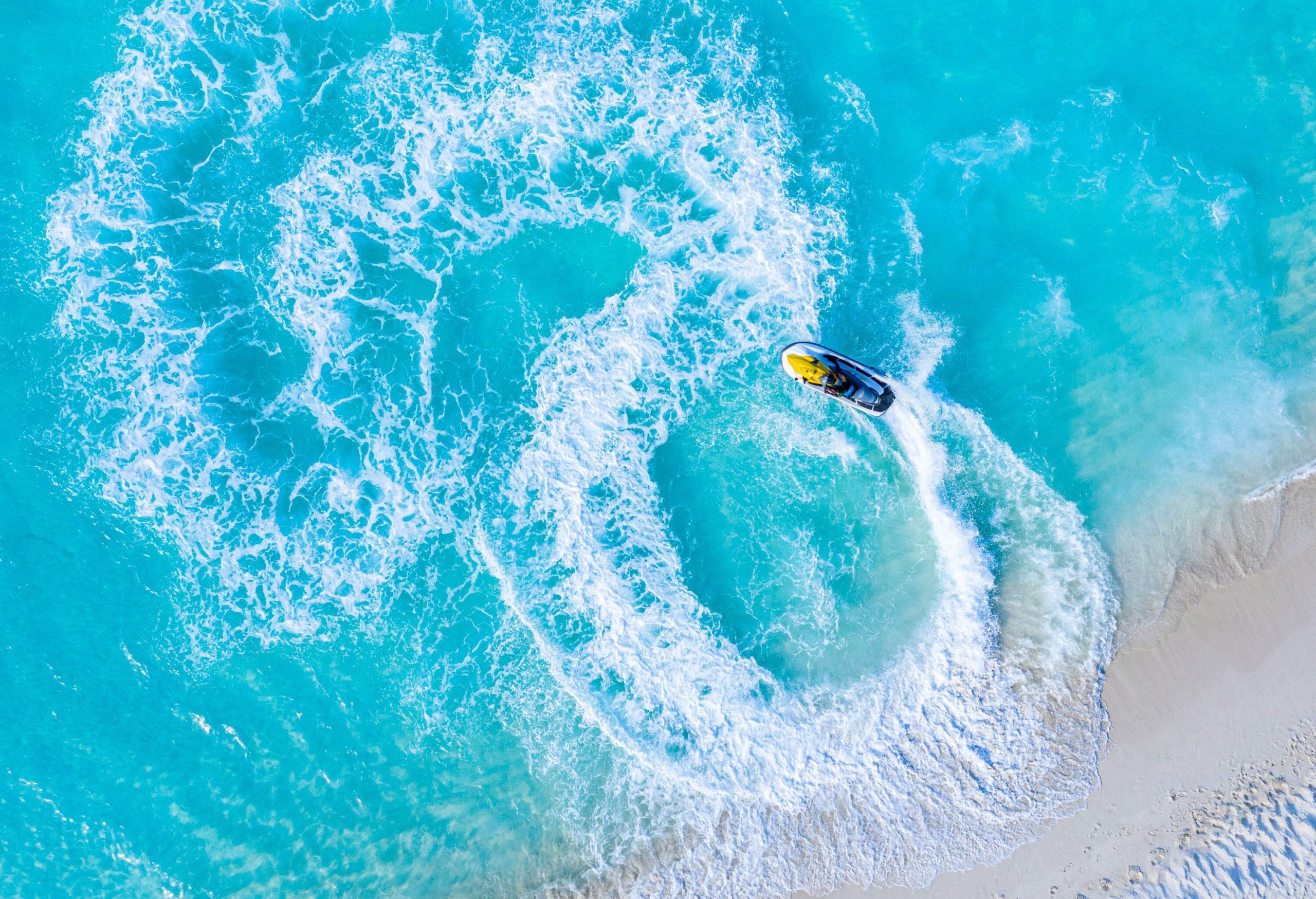 Waves are created by a jetski racing in circles on a clear beach.
