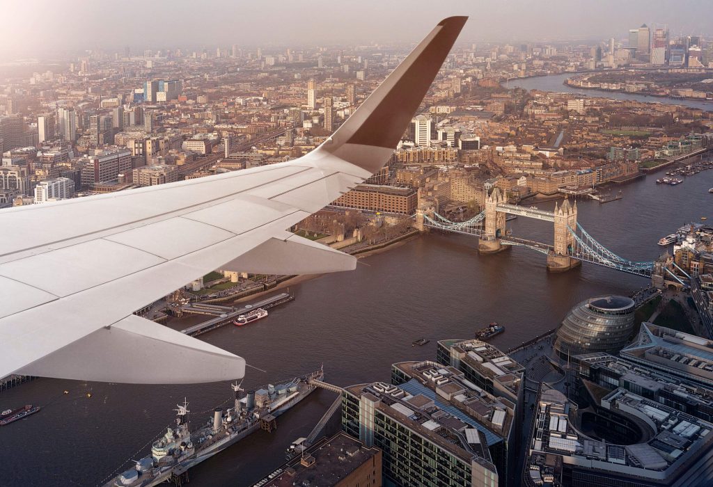 In the foreground, the wing of an airplane flying above the city of London and River Thames.