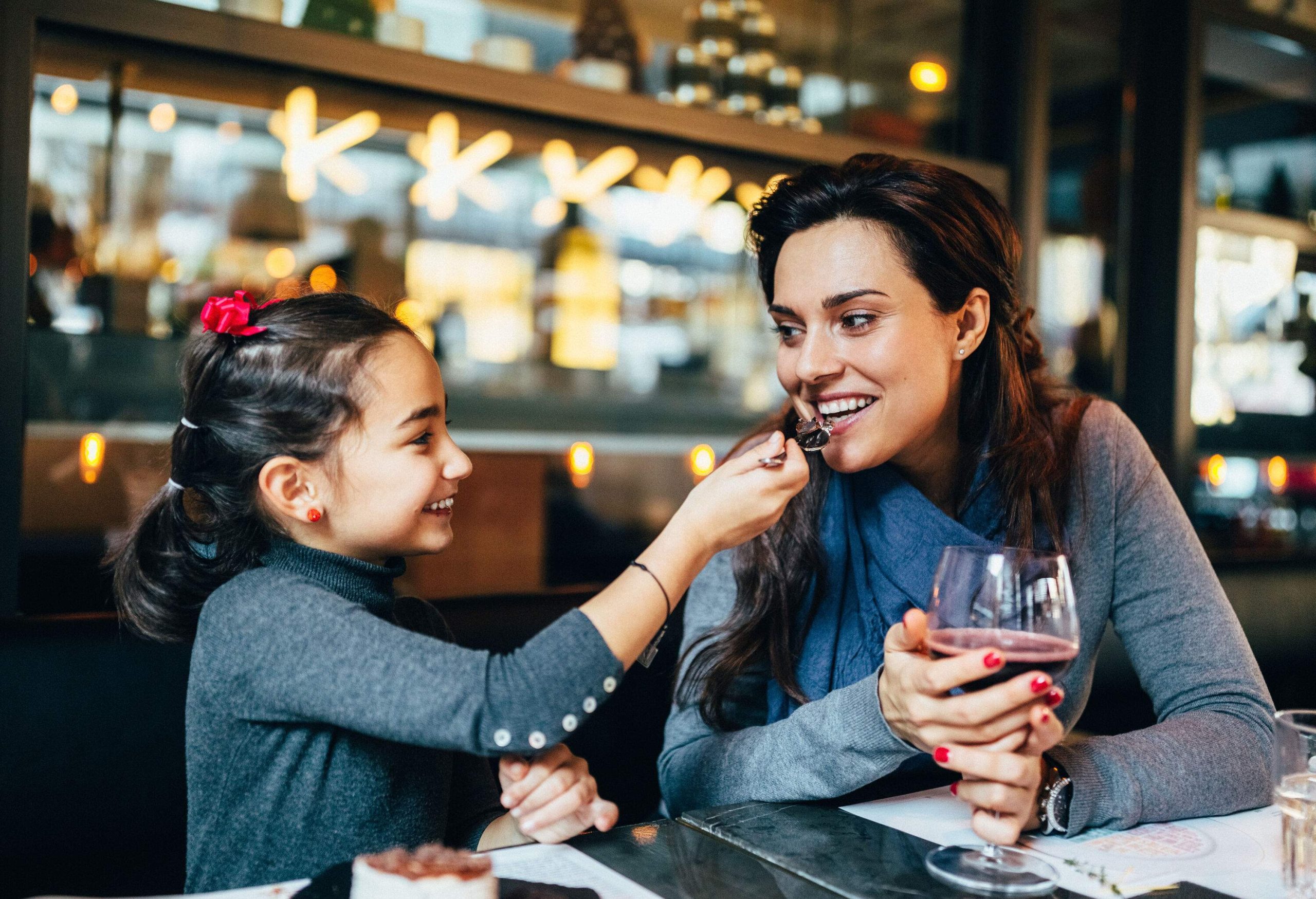A happy mother and daughter share a dessert at a restaurant.