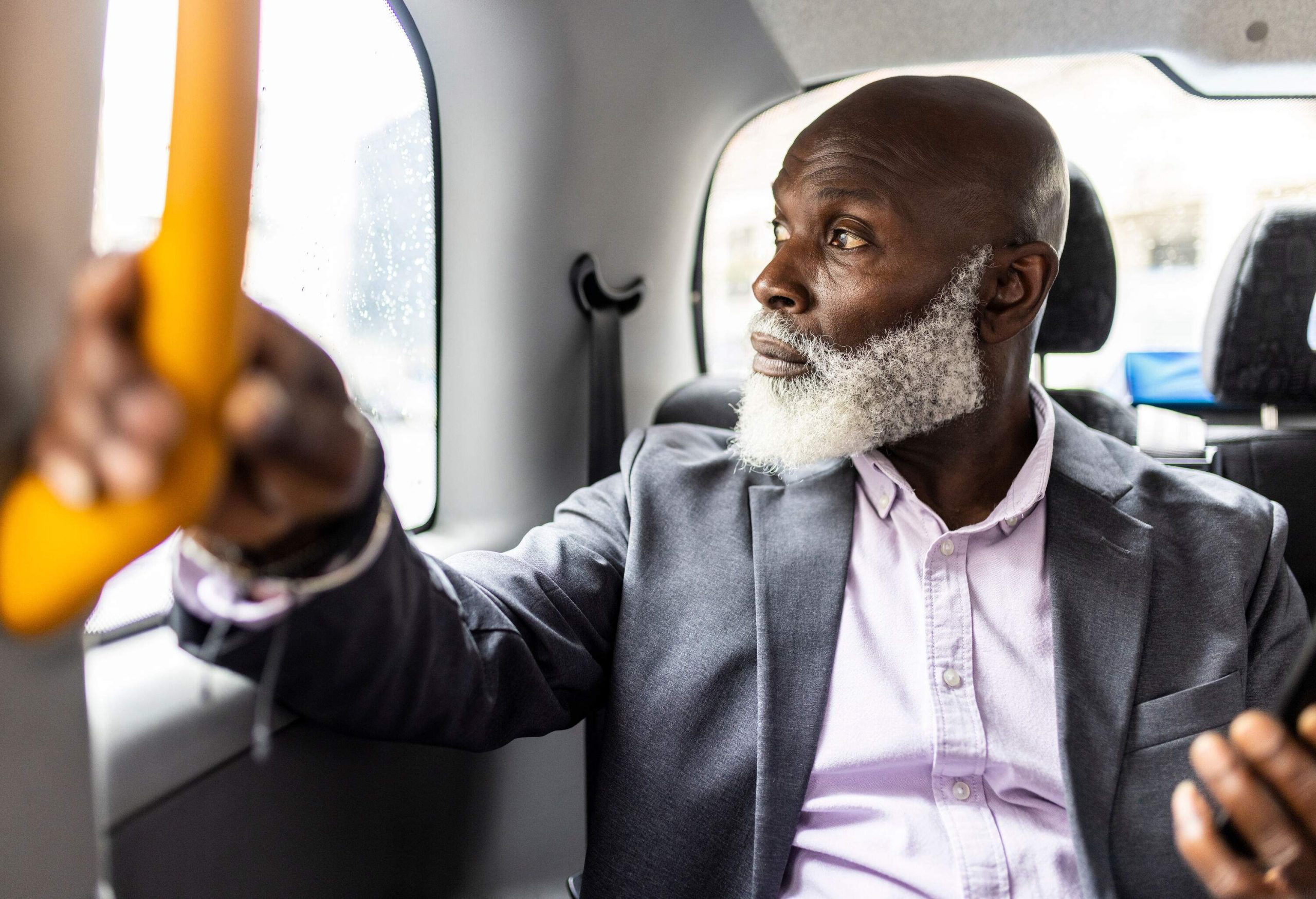 A man with a scraggly white beard peering out the window of a car.