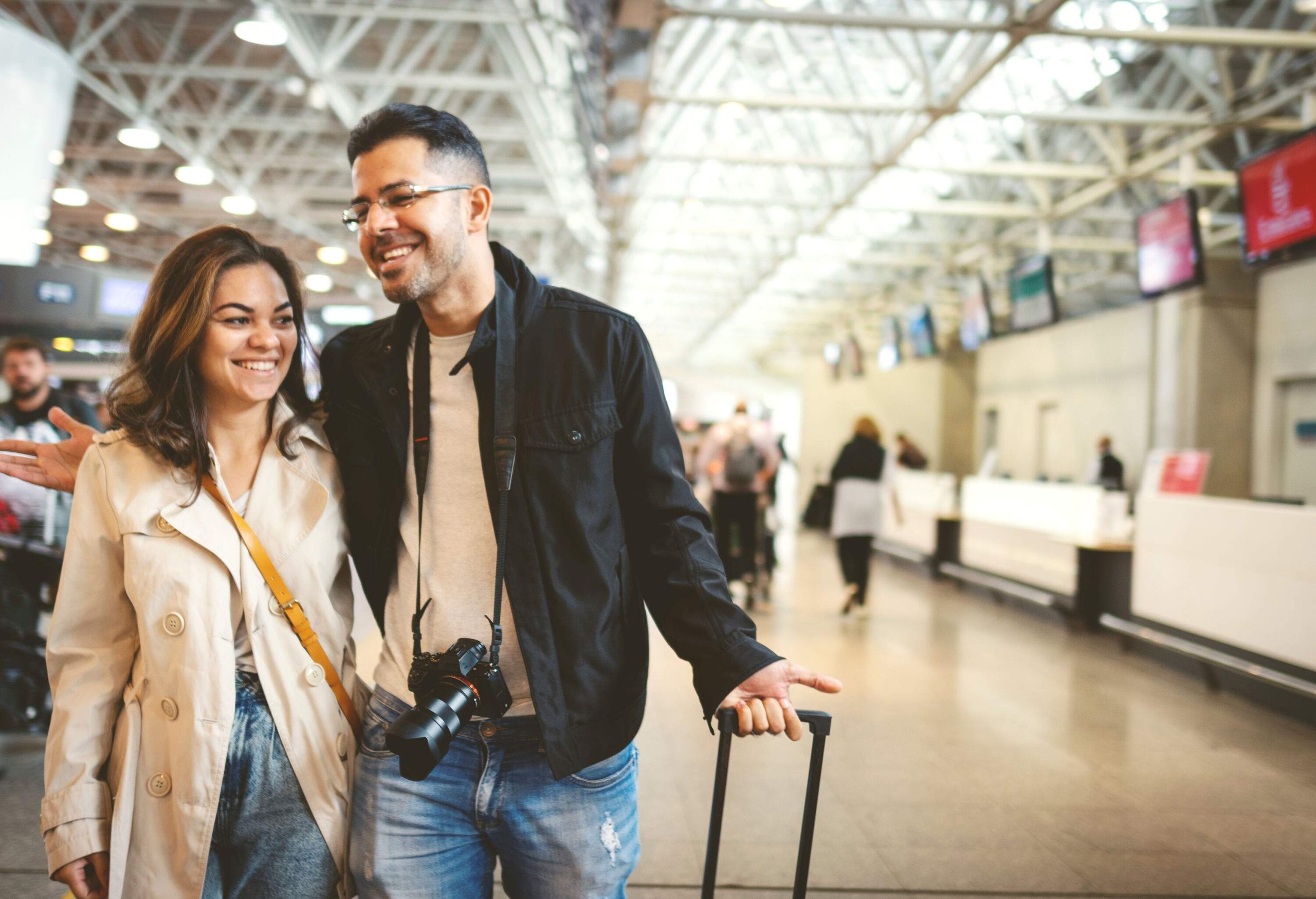 A happy couple walking through a terminal with their luggage in tow.