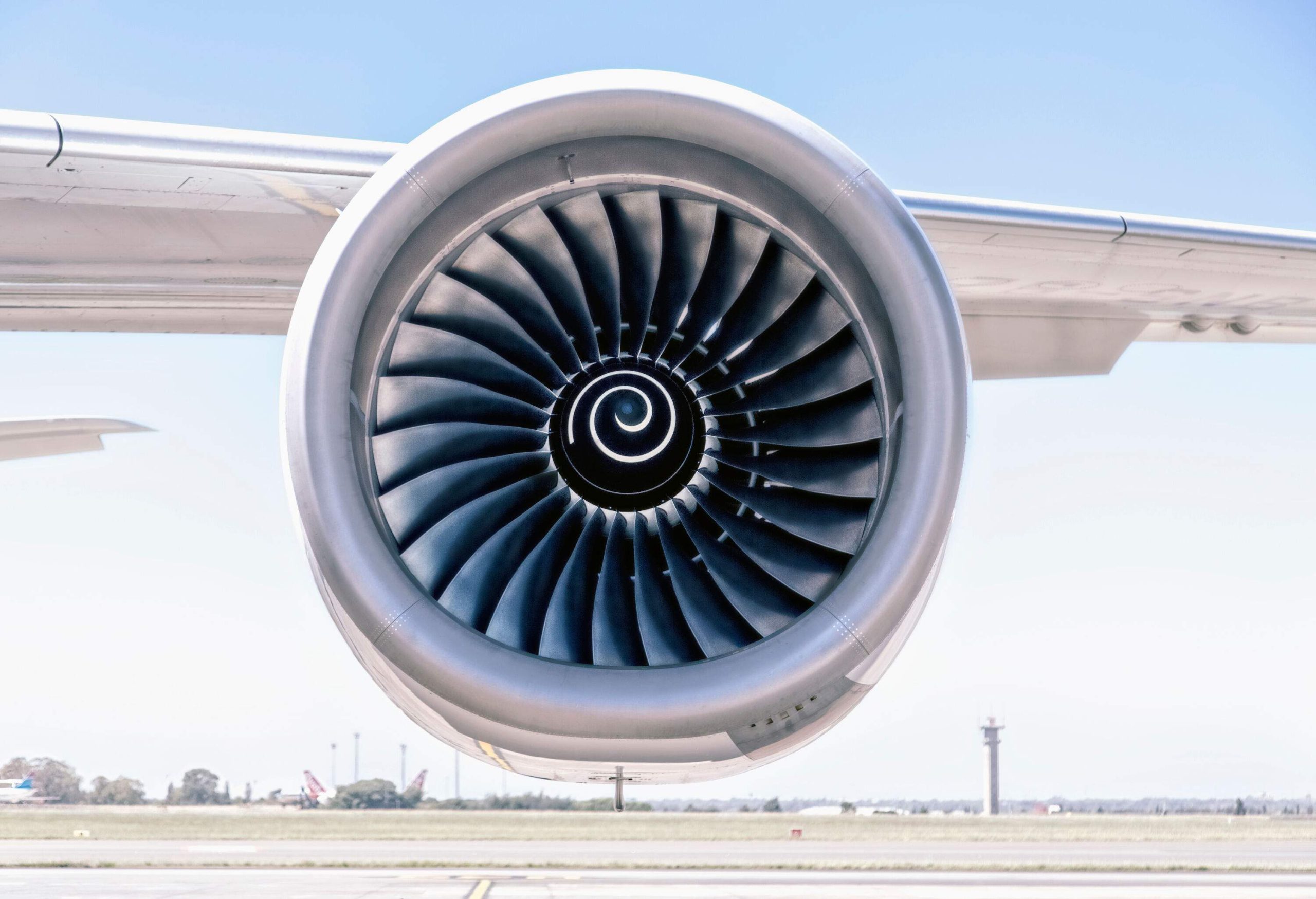 An aircraft engine attached to the wings against the whitish blue sky.