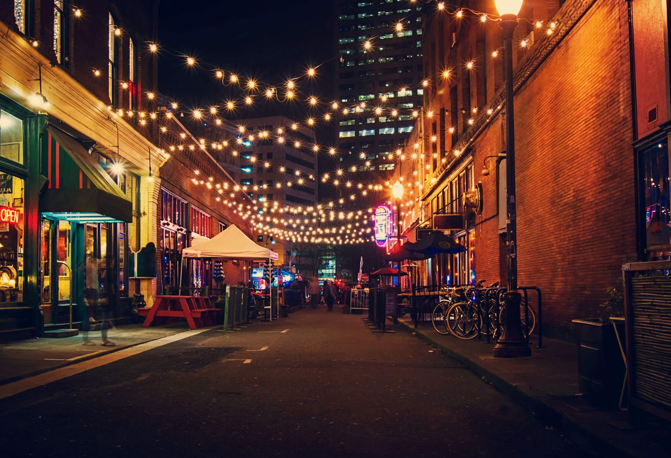 Lit up string lights hanging over a street lined with pubs and restaurants.