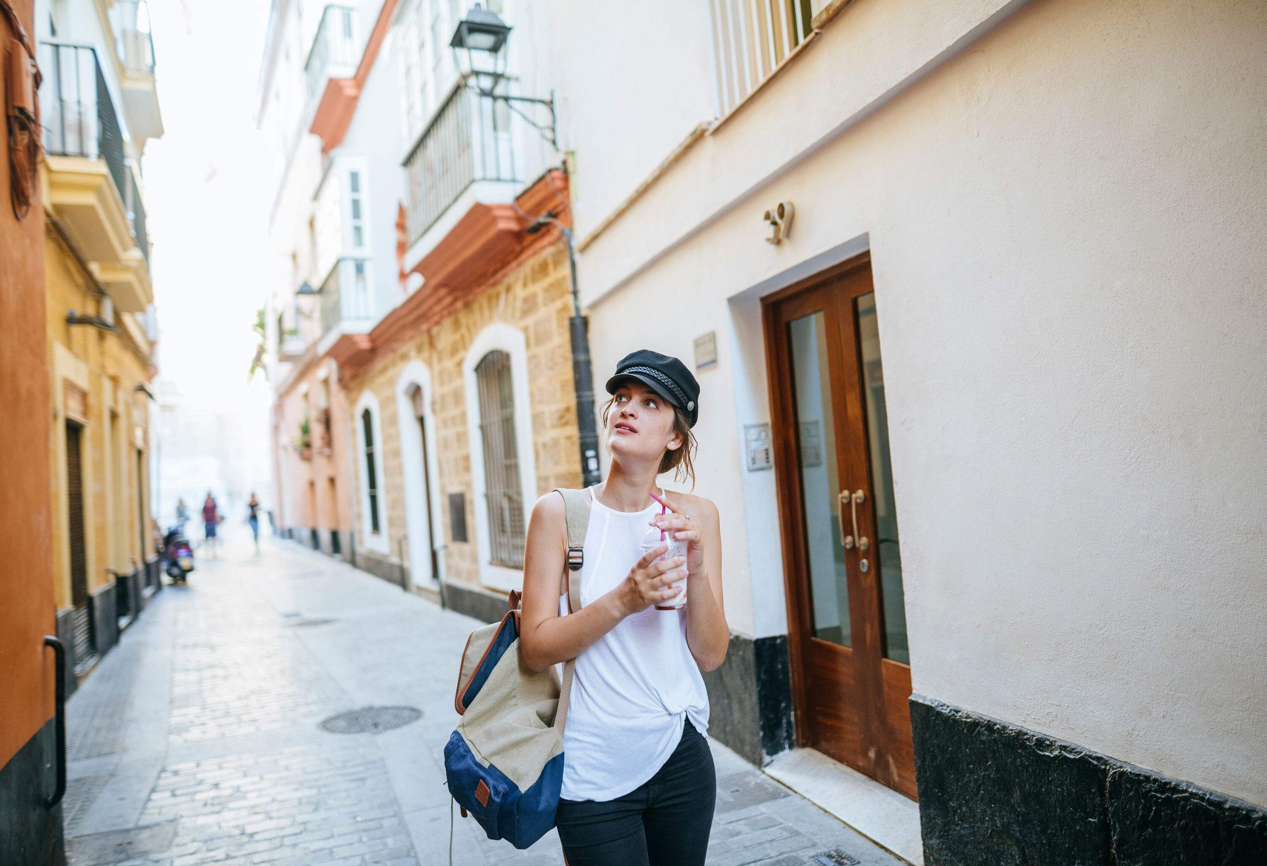 A young female tourist with a drink in her hands strolling along an alleyway.