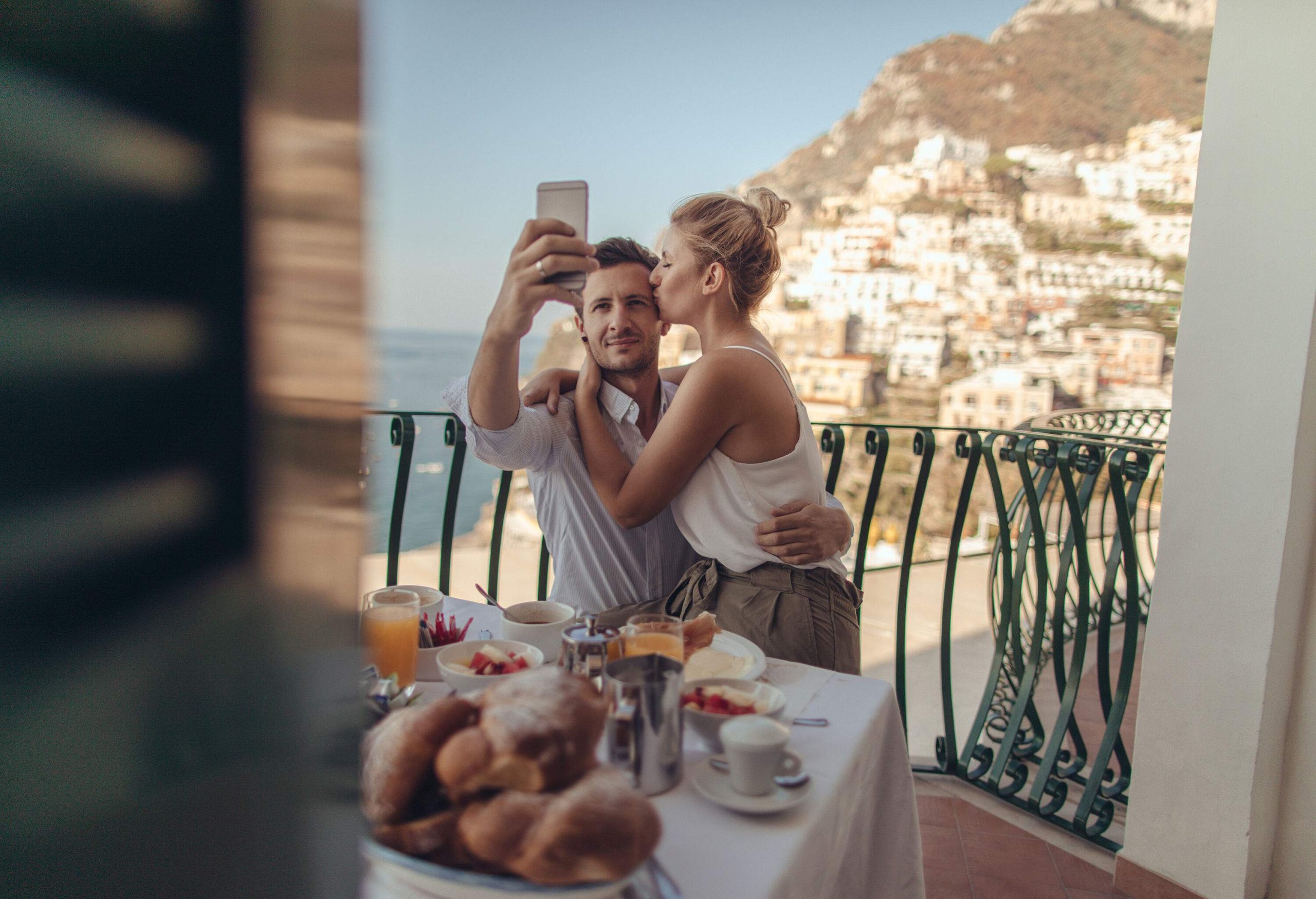 A couple with their breakfast on the balcony and taking a selfie.