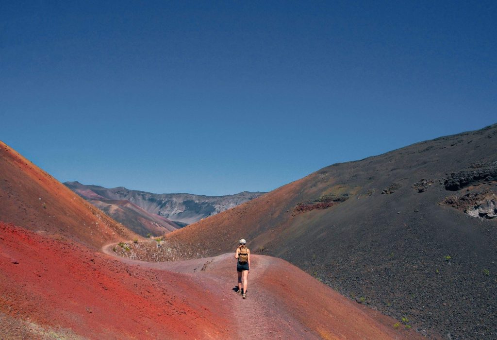 A girl embarks on an adventure, hiking through the mesmerizingly colourful sand slopes of Haleakalā National Park.