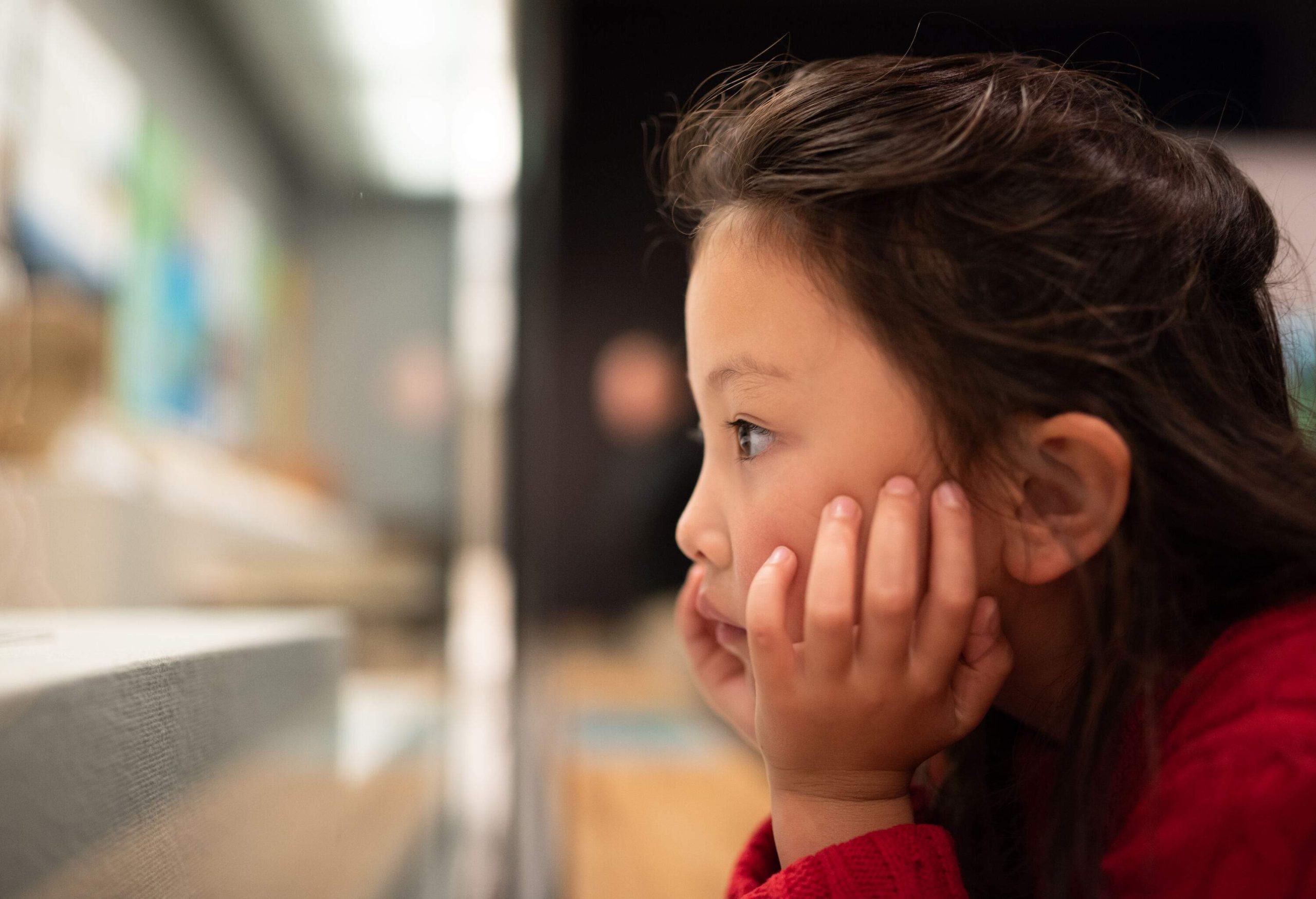 A little girl stares blankly with her head resting on her hands.