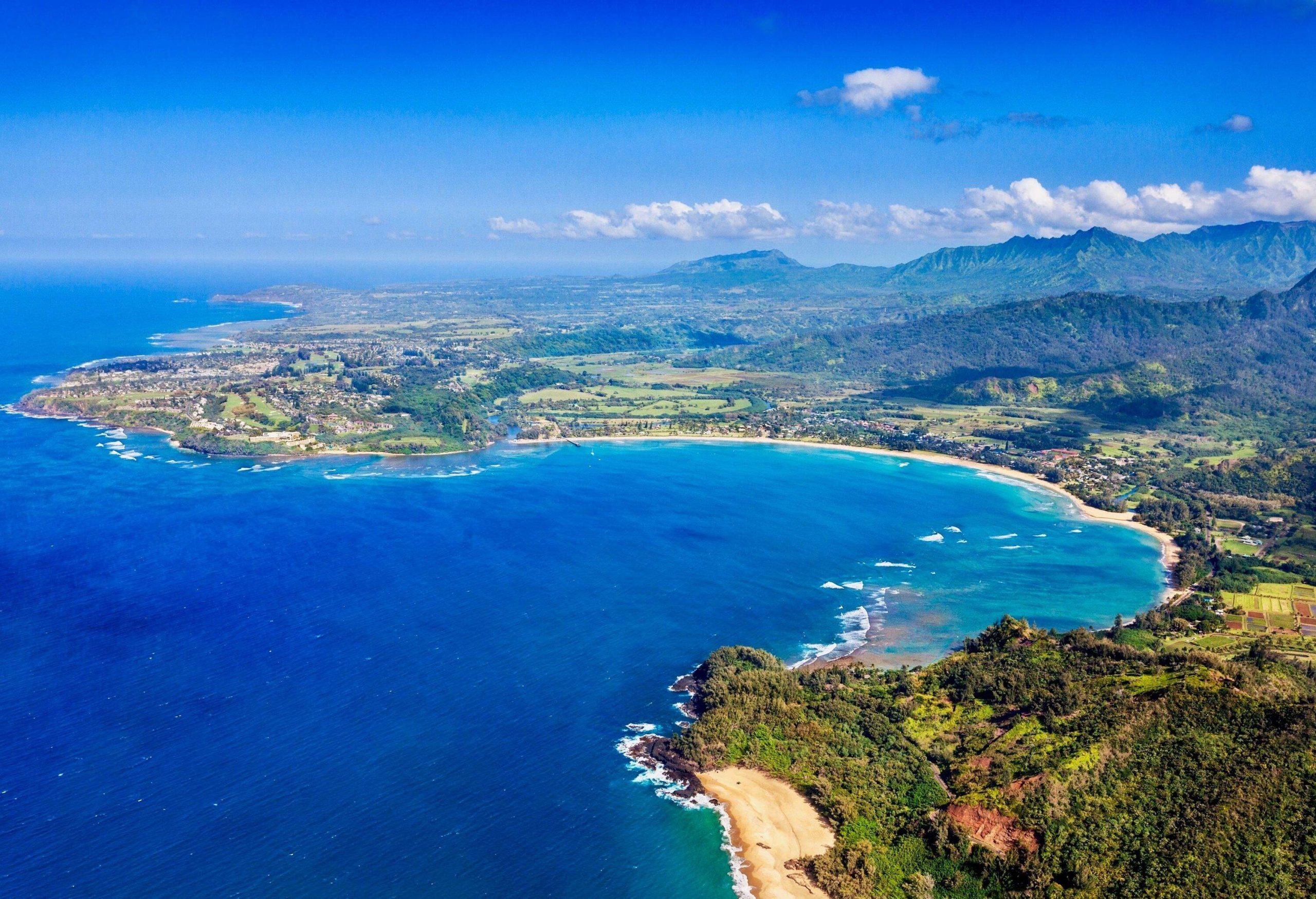 Aerial view of a lush coastal island surrounded by the blue sea under the cloudy blue sky.