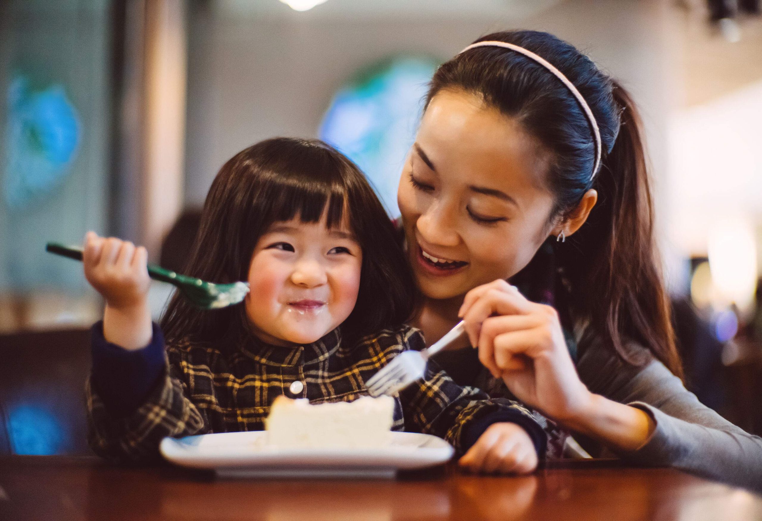 A mother and her little daughter sharing a slice of cheesecake.