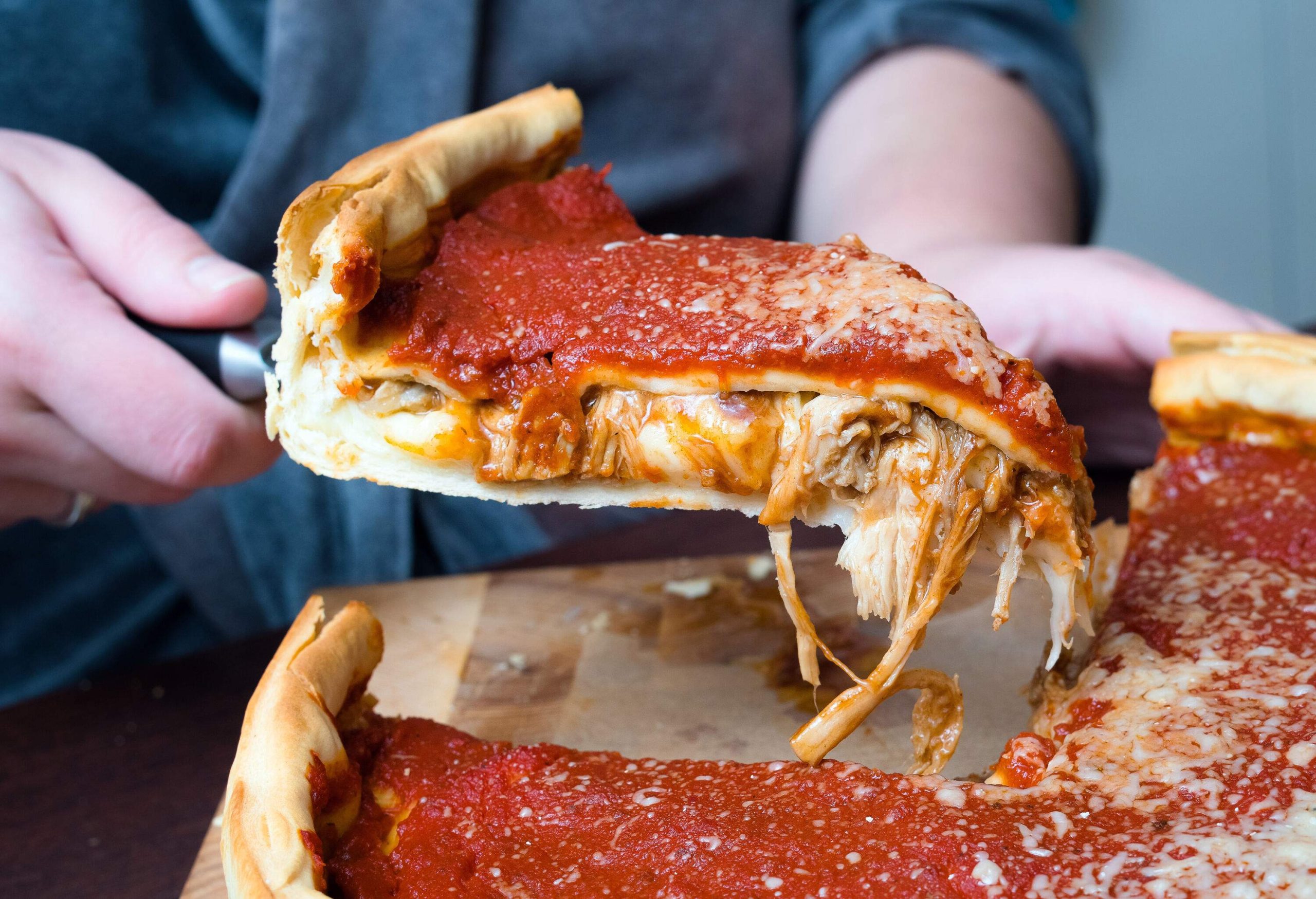 A woman's hands skillfully slice into a scrumptious Chicago-style deep dish pizza, brimming with gooey Italian cheese, rich tomato sauce, and succulent beef mince.