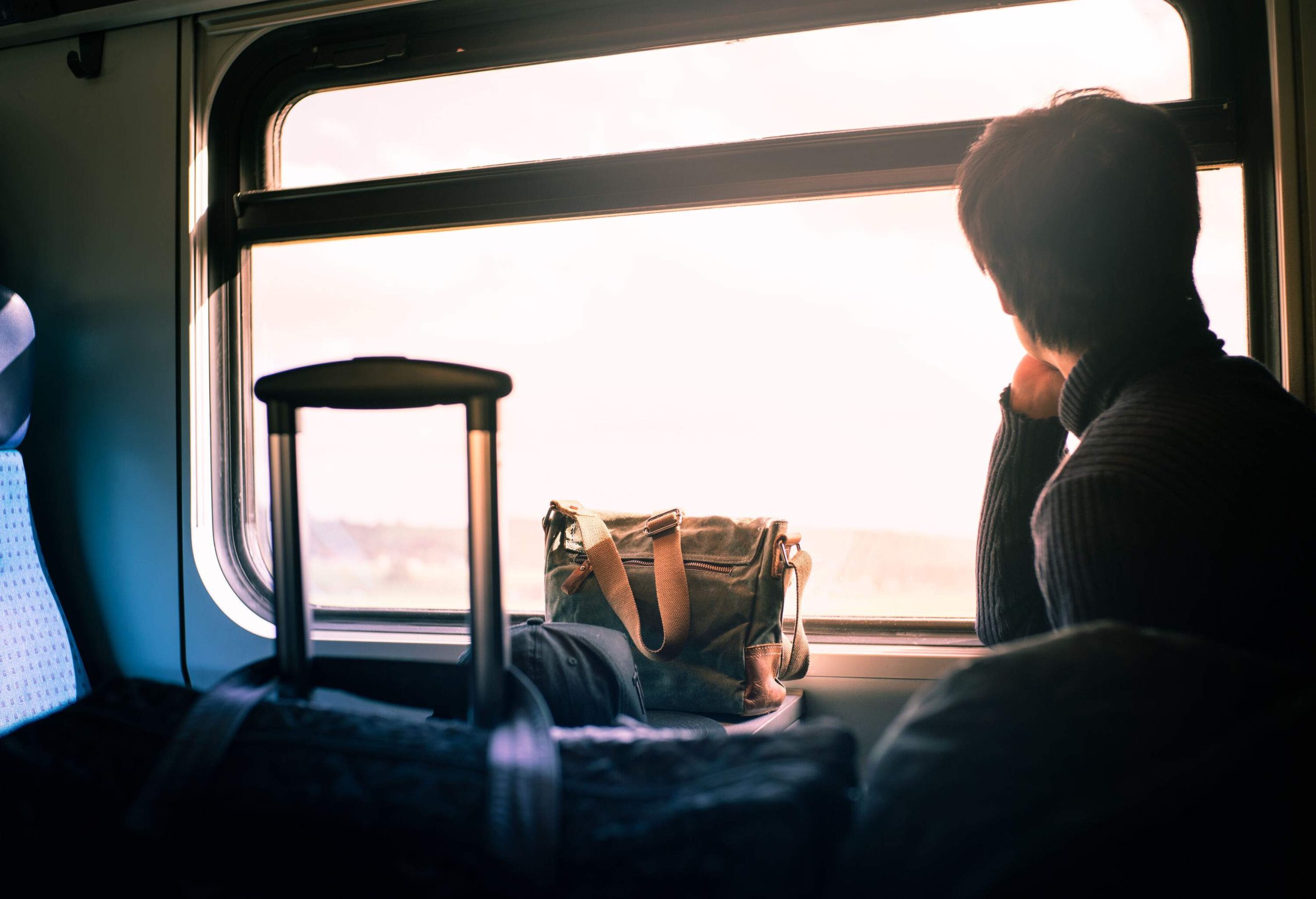 A male traveller rides the train with his luggage and looks through the window.