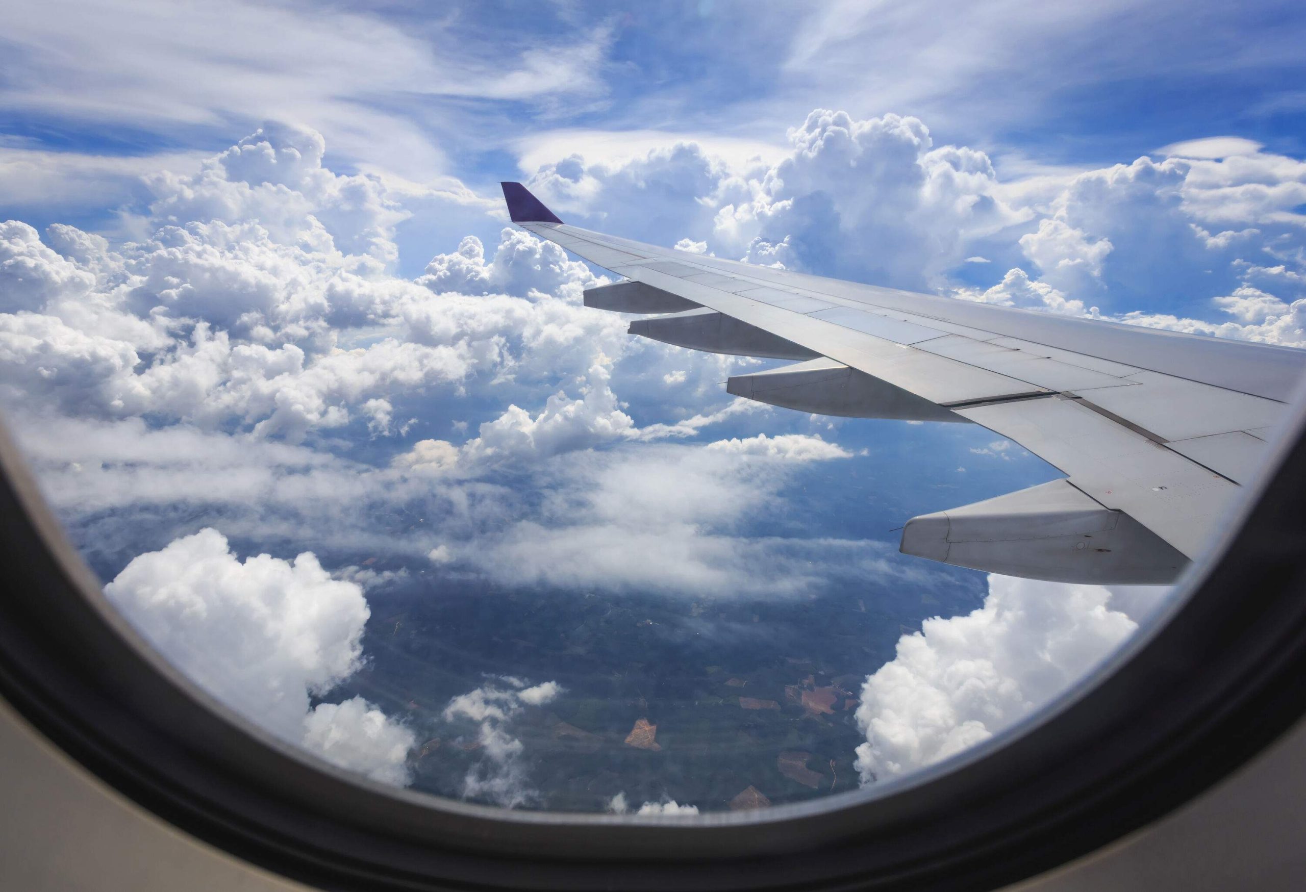 The wing of an airplane, the white clouds on the blue sky viewed on the plane's window.