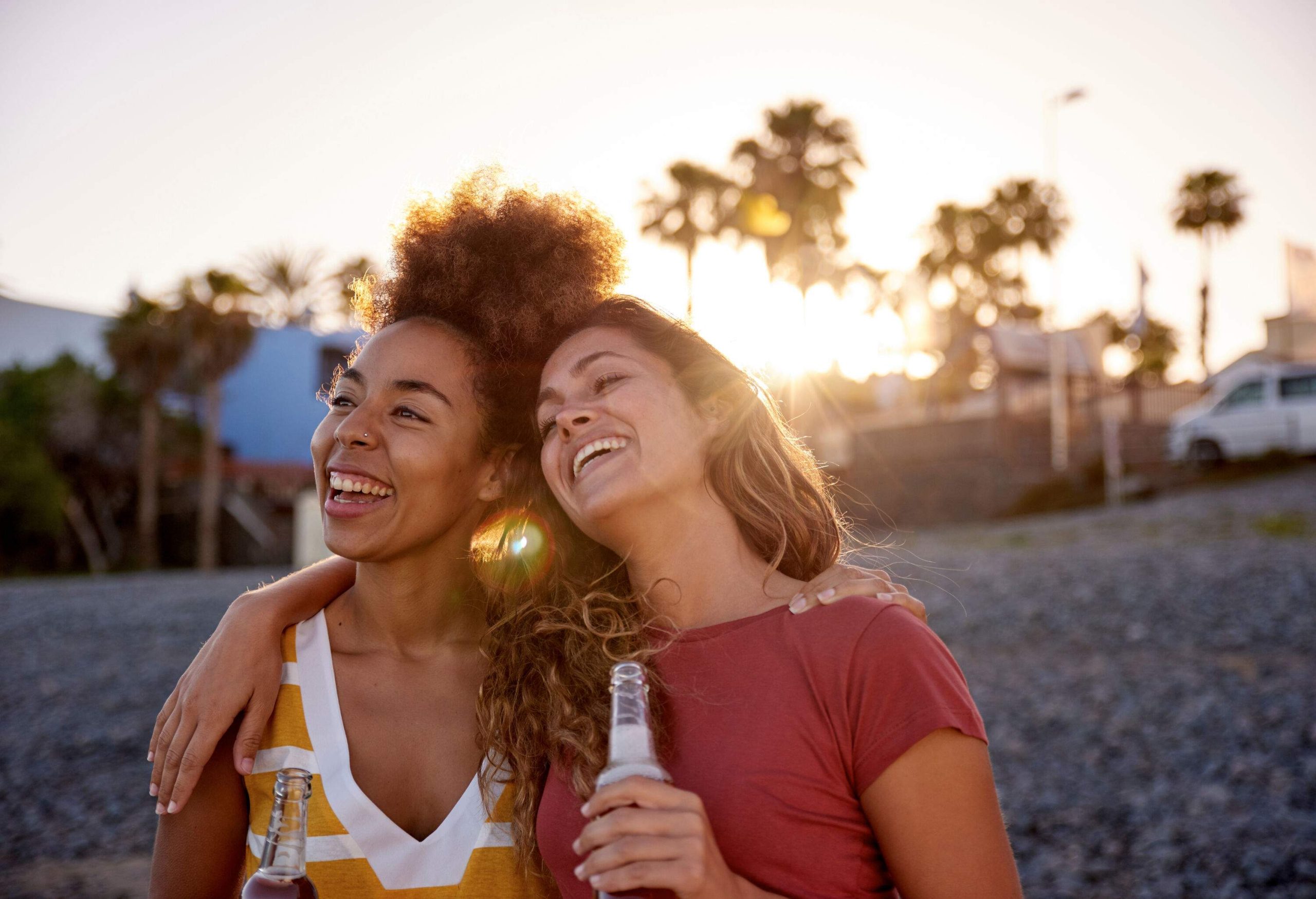 Two happy women standing on the beach, each holding a bottle of beer.