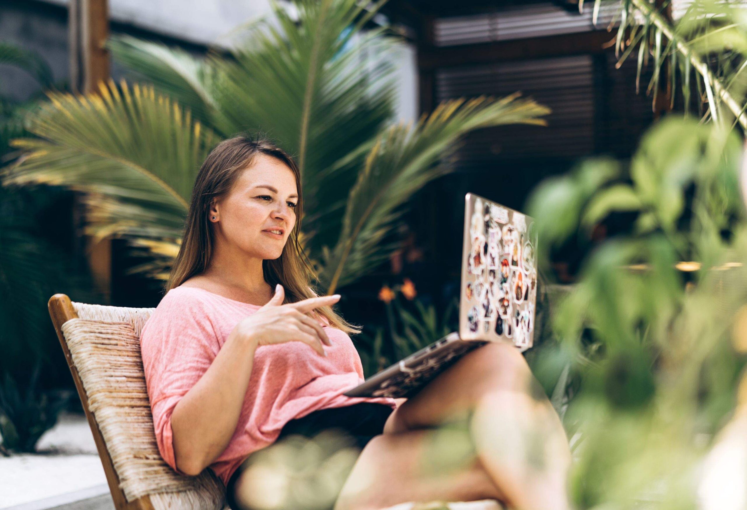 A woman sitting in front of a laptop in the beach cafe. Business trip or vacation in a high class tropical resort. Online shopping, booking, freelance working