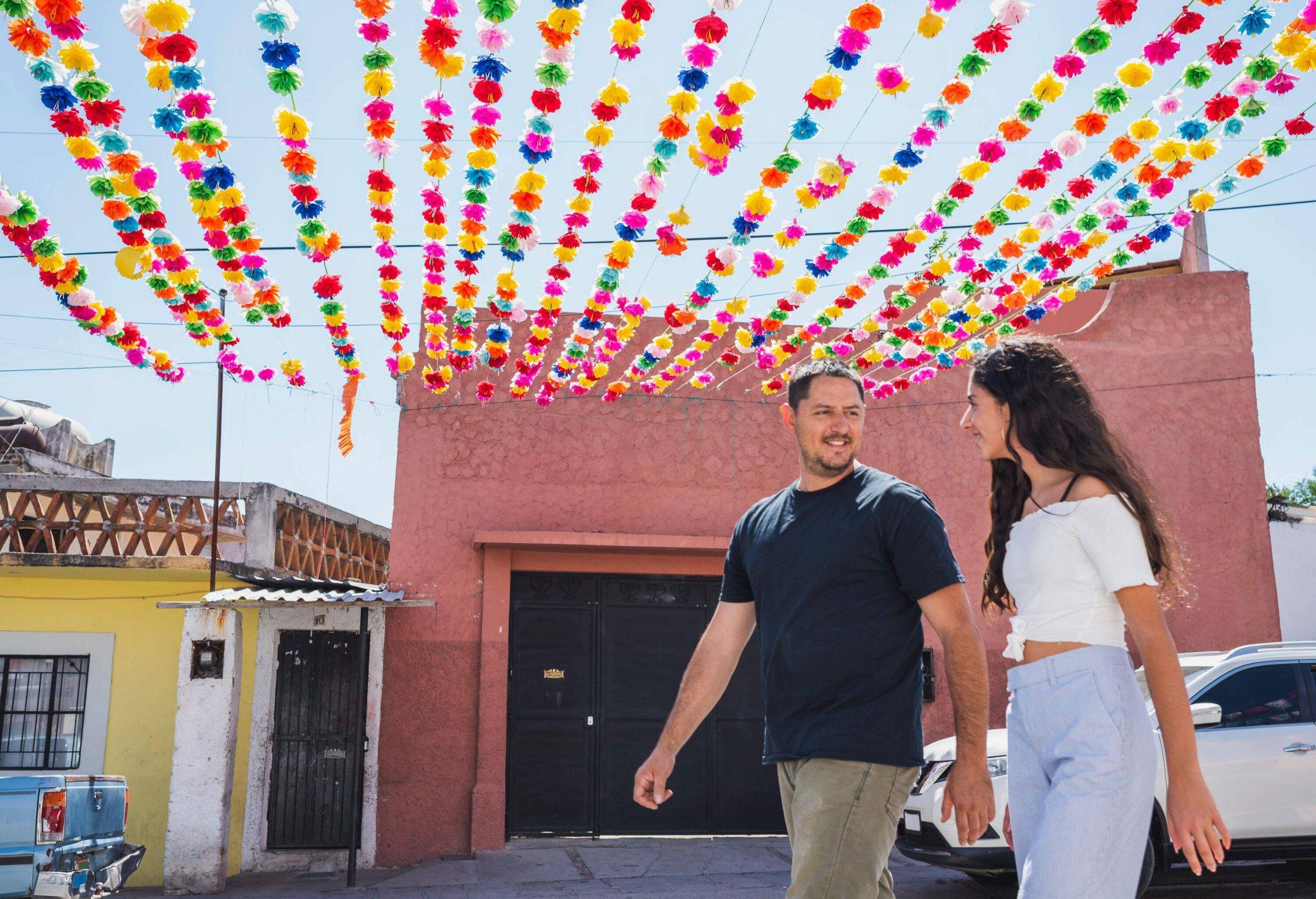 A man and a woman walking down the street under colourful paper flowers.