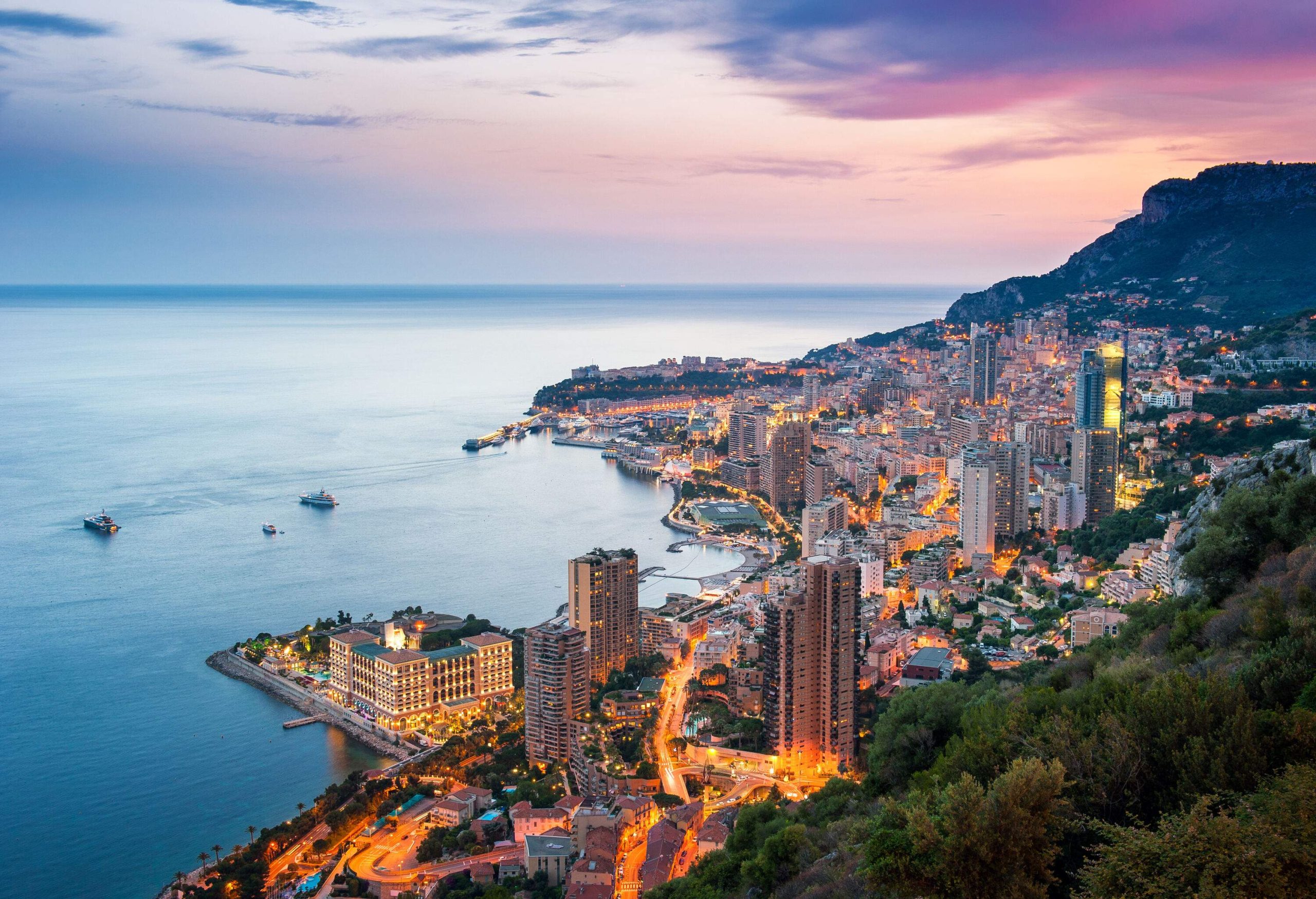 A coastal metropolis comes to life with towering lit skyscrapers as a gorgeous sunset casts its warm hues over the huge expanse of the sea.