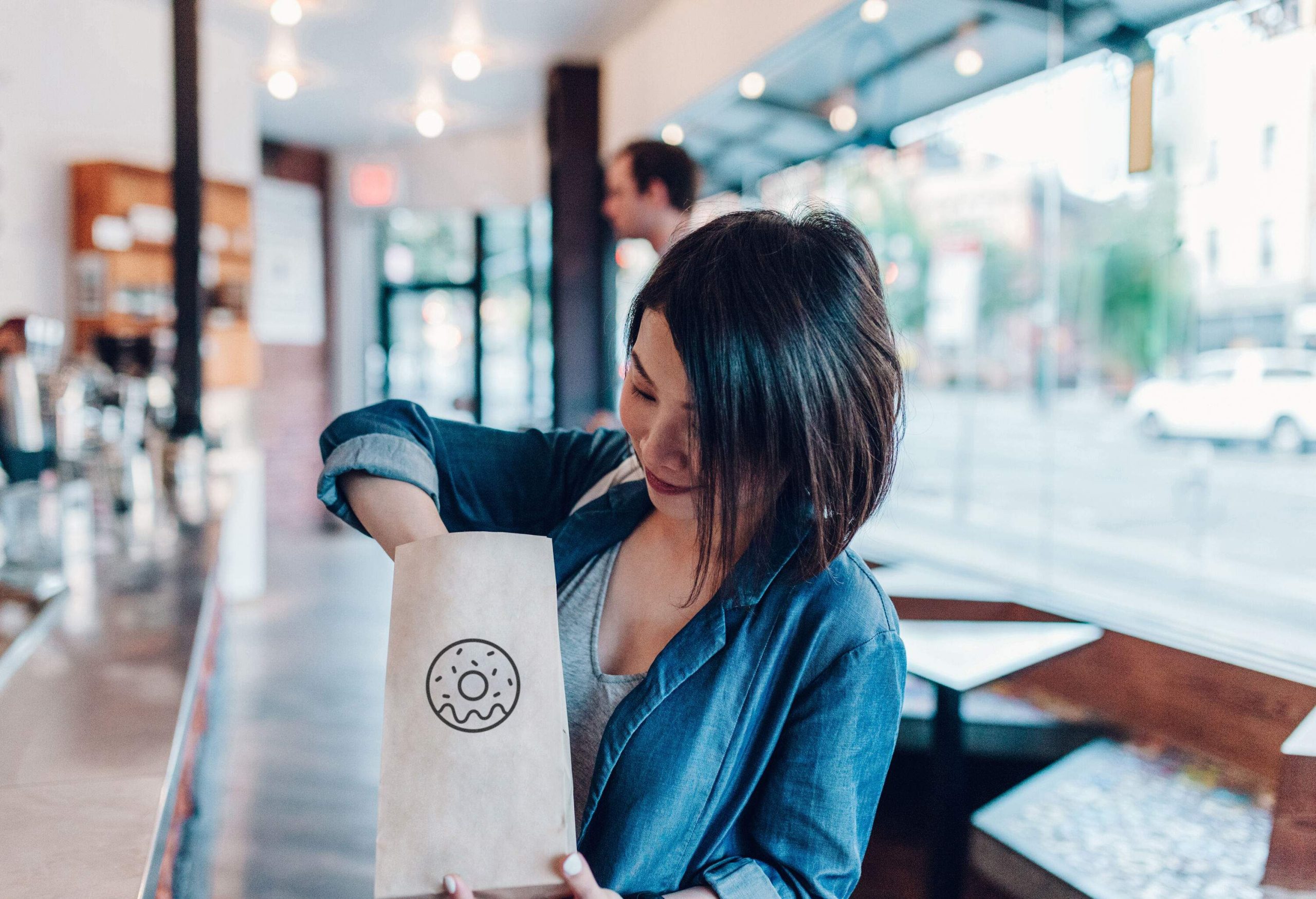 A young woman delving into a brown paper bag with an outline of a doughnut on it.