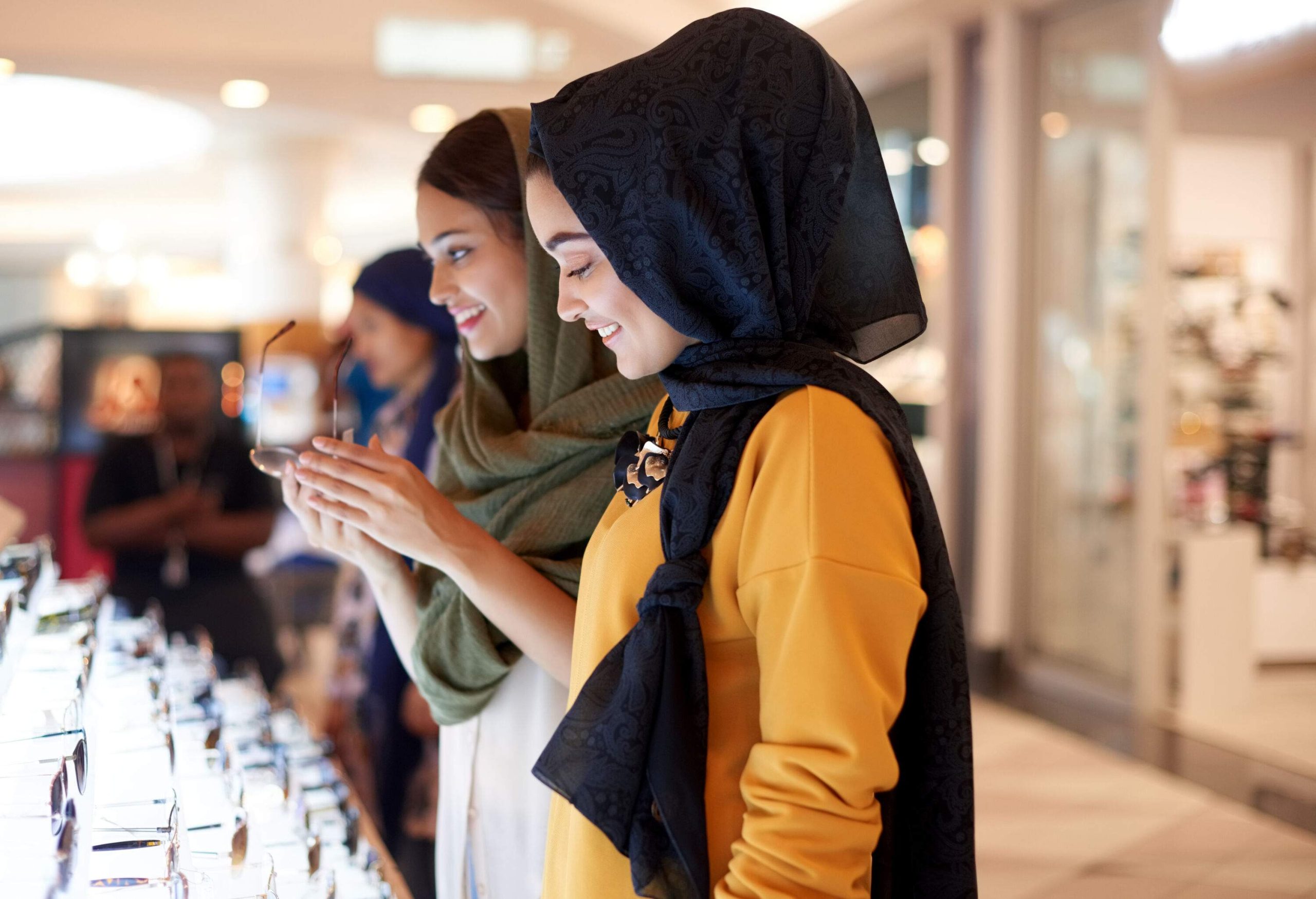 Young women wearing head coverings checking out a display of sunglasses.