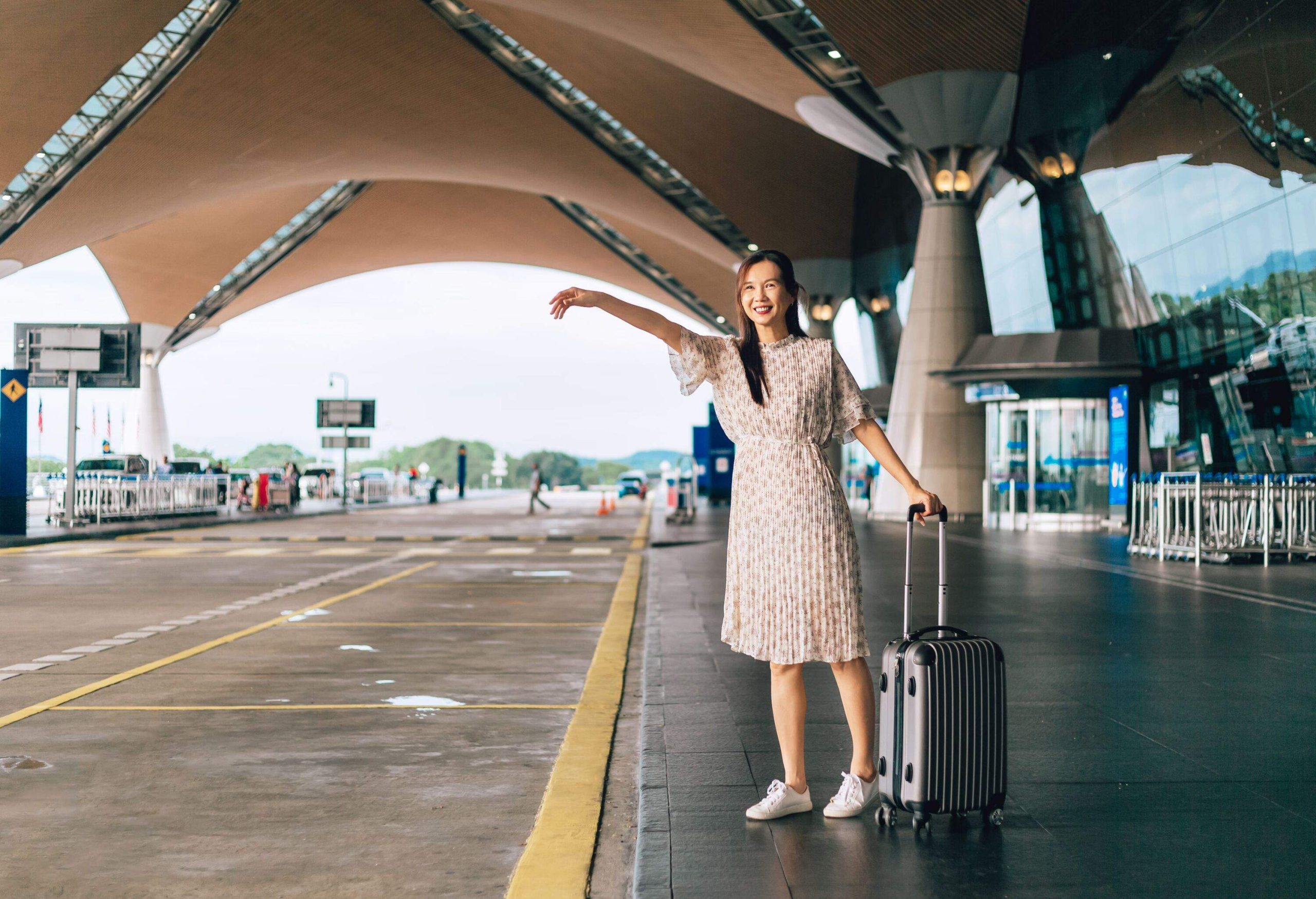 Young woman in casual clothing stretched out arm looking at the street to stop taxi in airport entrace