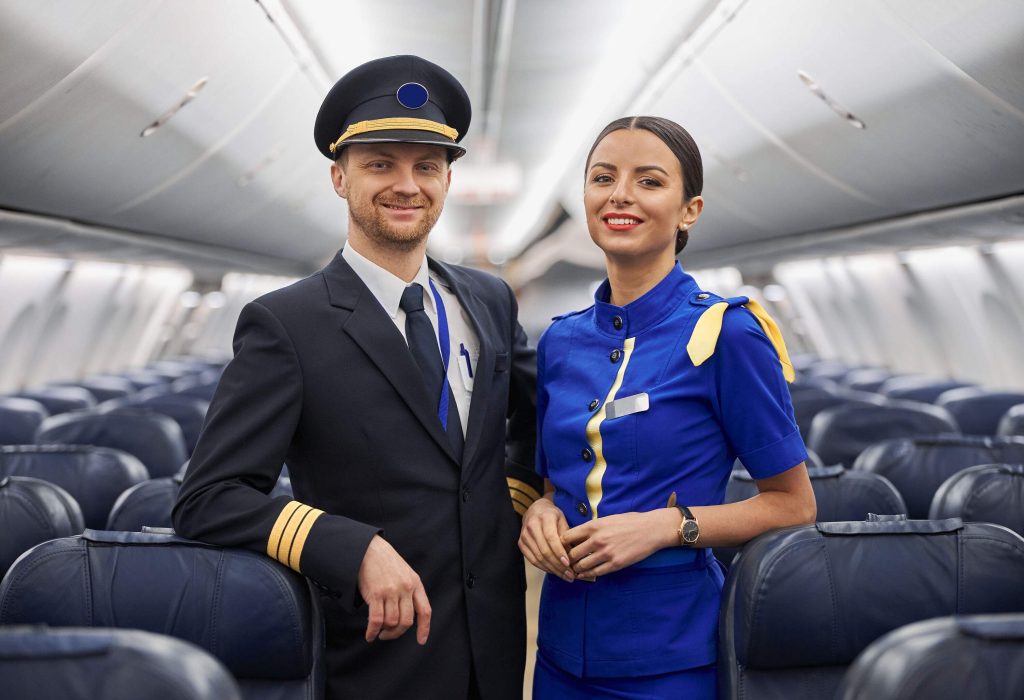 A pilot and a cabin crew in uniform standing in the middle of the aircraft's aisle.