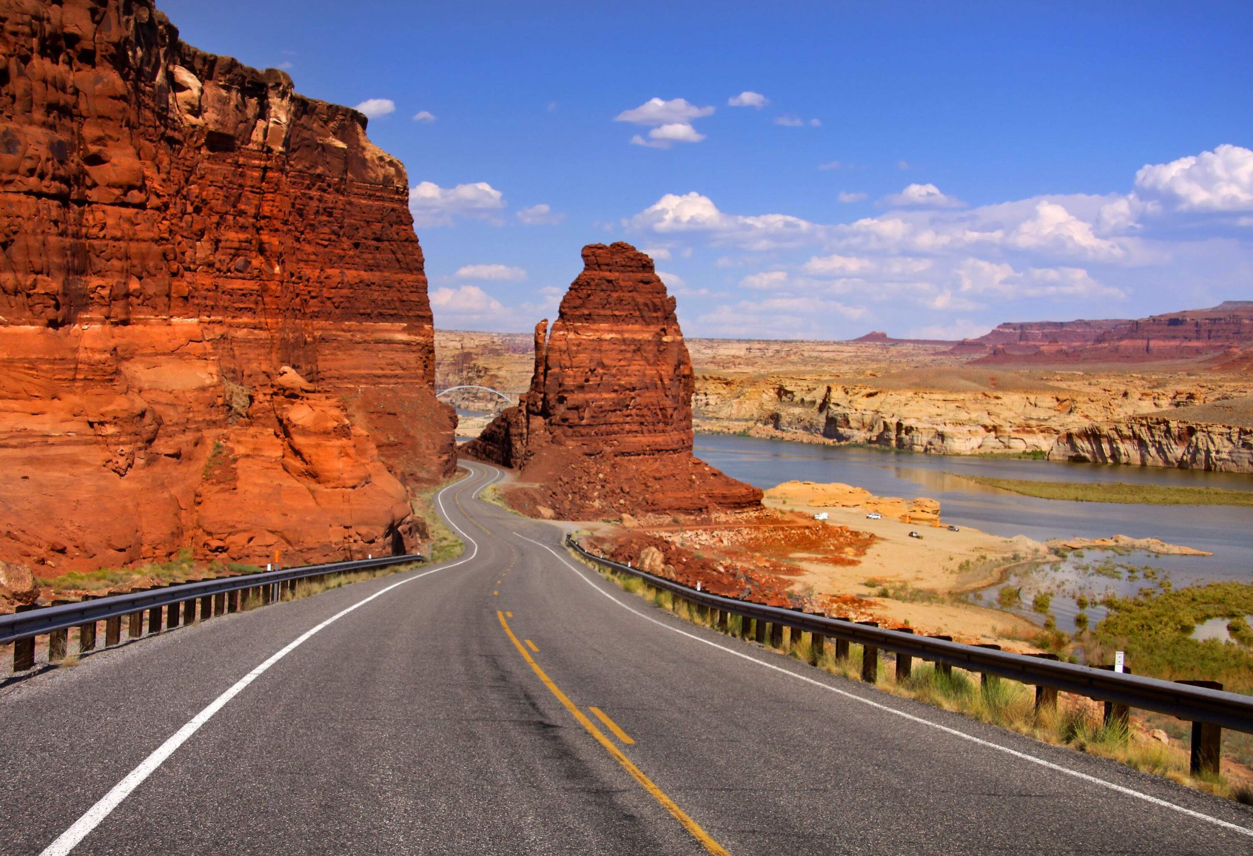 An empty road between the red and orange sandstone canyons with riverfront views.