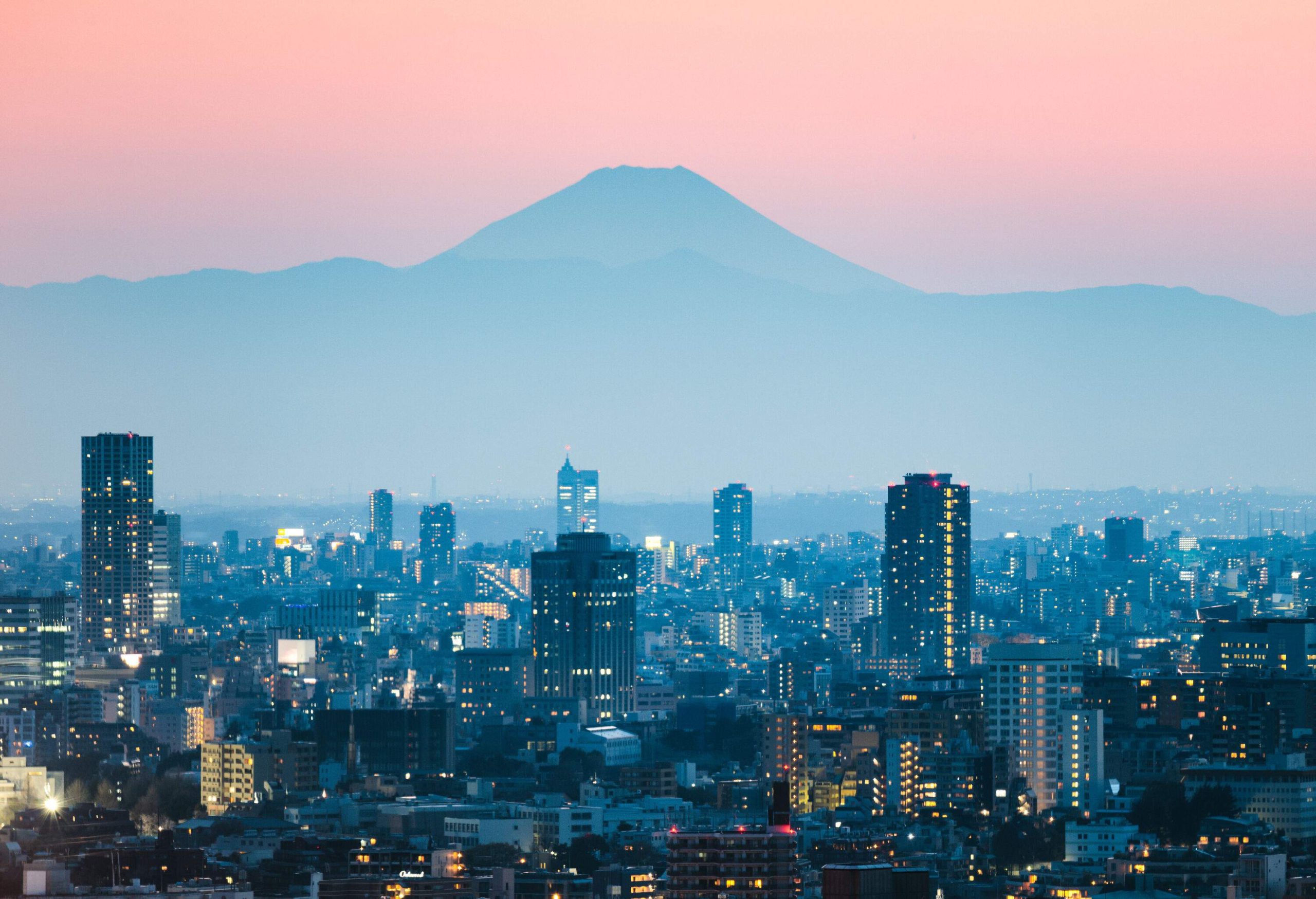 The iconic Mount Fuji is in the backdrop against the lit cityscape.