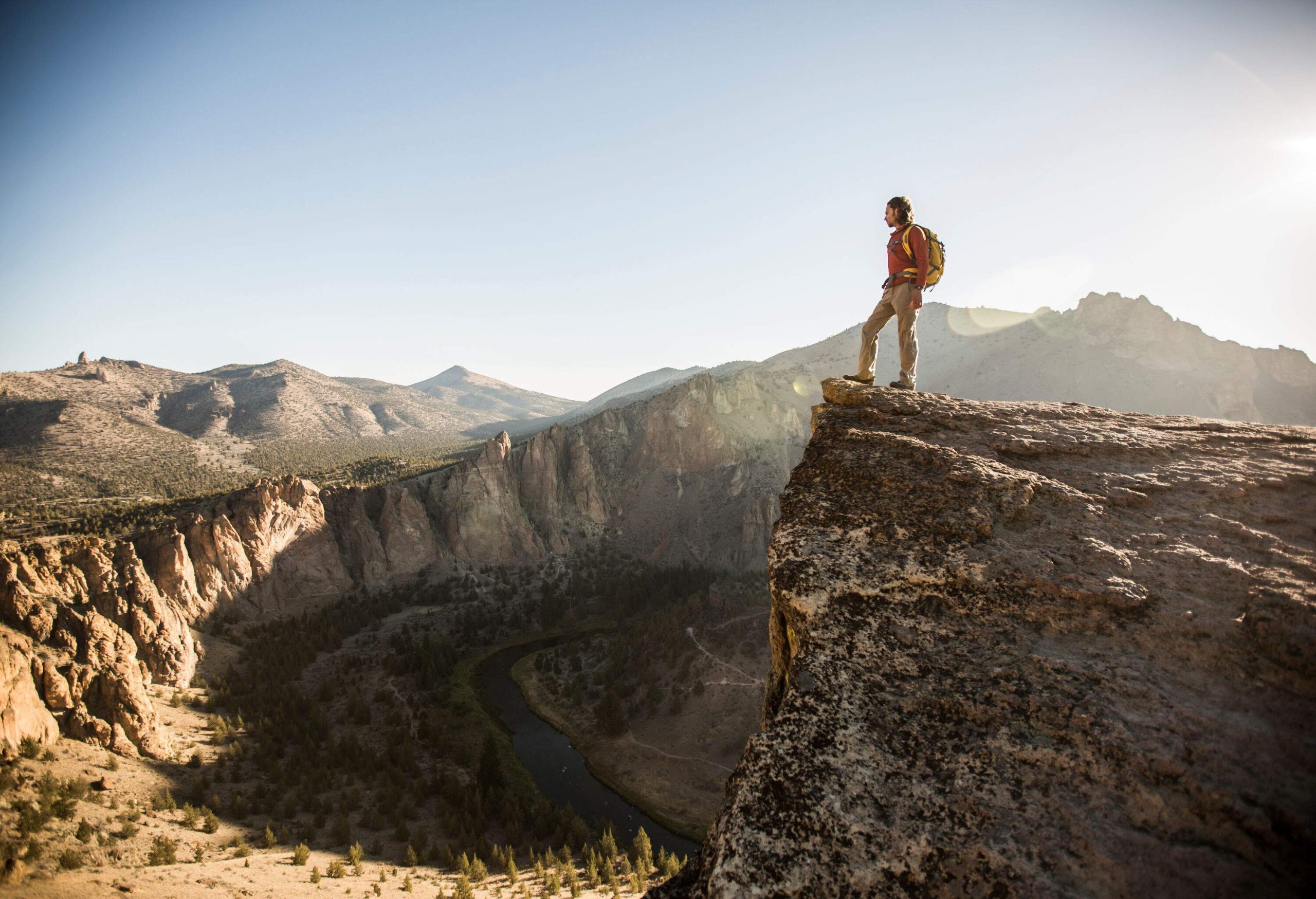 Hiker standing on the edge of a cliff while looking down at the river along the steep canyons.