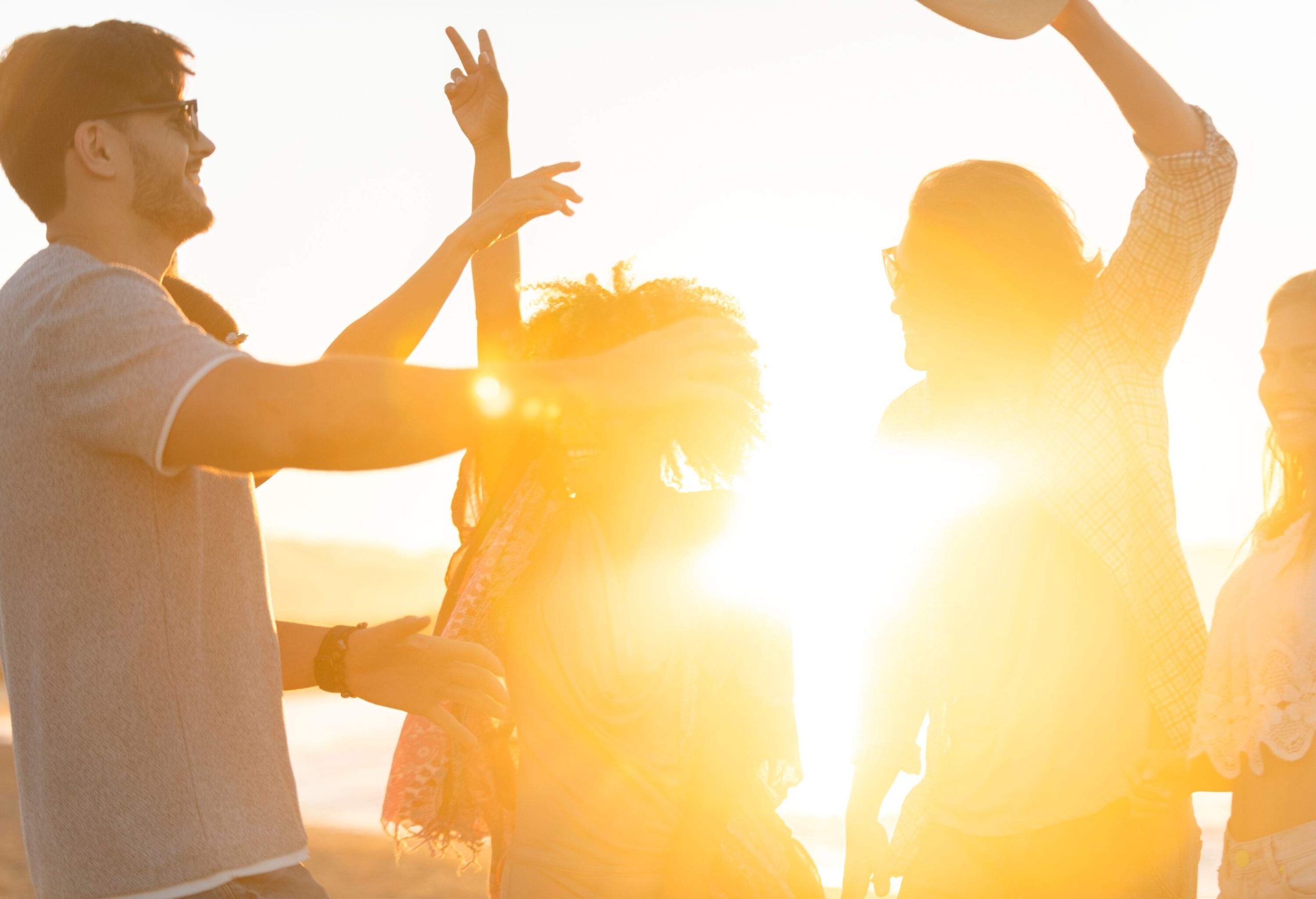 A group of young people dancing and having a good time on the beach at sunset.