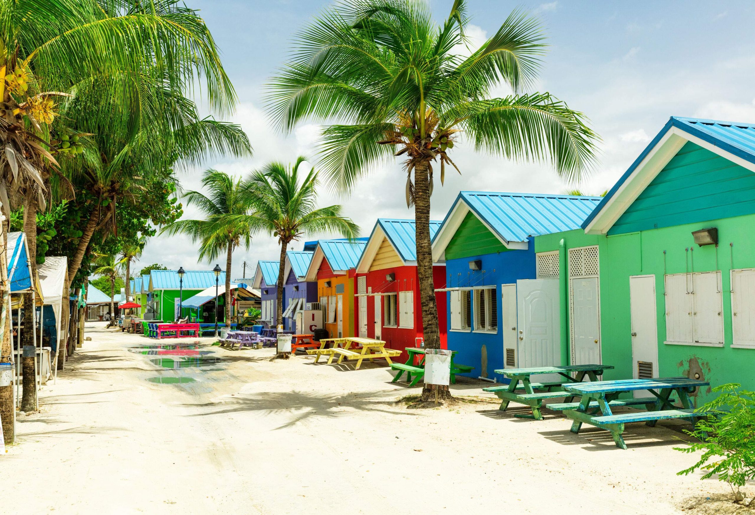 Rows of colourful houses gracefully perch on the soft white sand, while swaying palm trees dot the landscape.