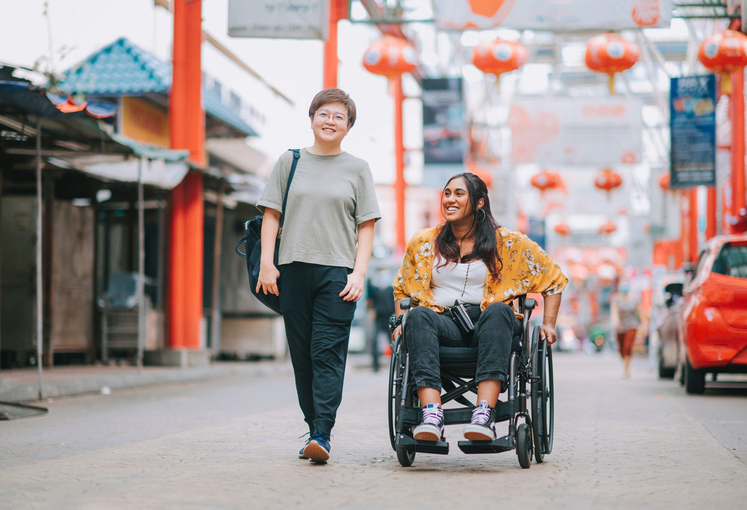 An adult woman walking beside a disabled female in a wheelchair down a city street.