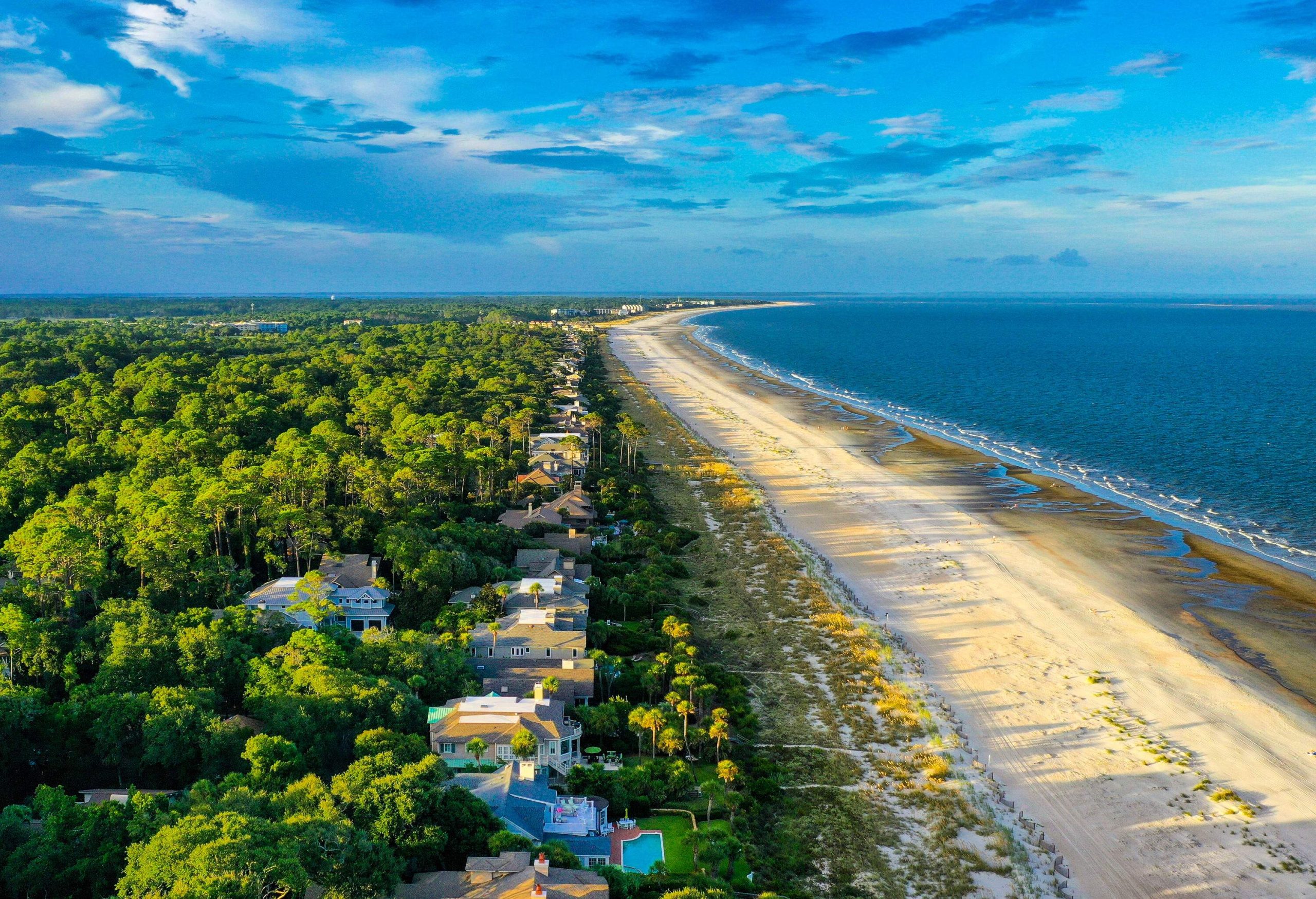 Aerial view of modern and luxury beach houses on a forested island with a sandy shore surrounded by the tranquil blue sea.