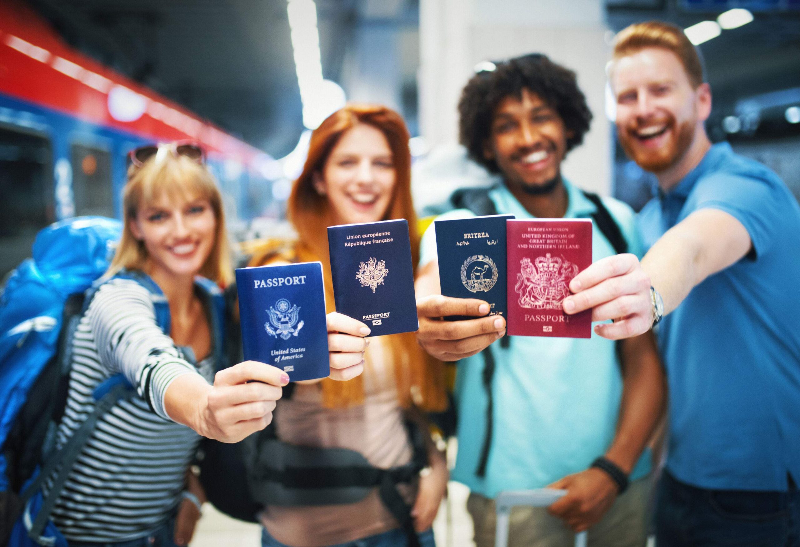 Closeup of group of young adults showing their passports to the camera. They are at a train station, ready for their summer trip.