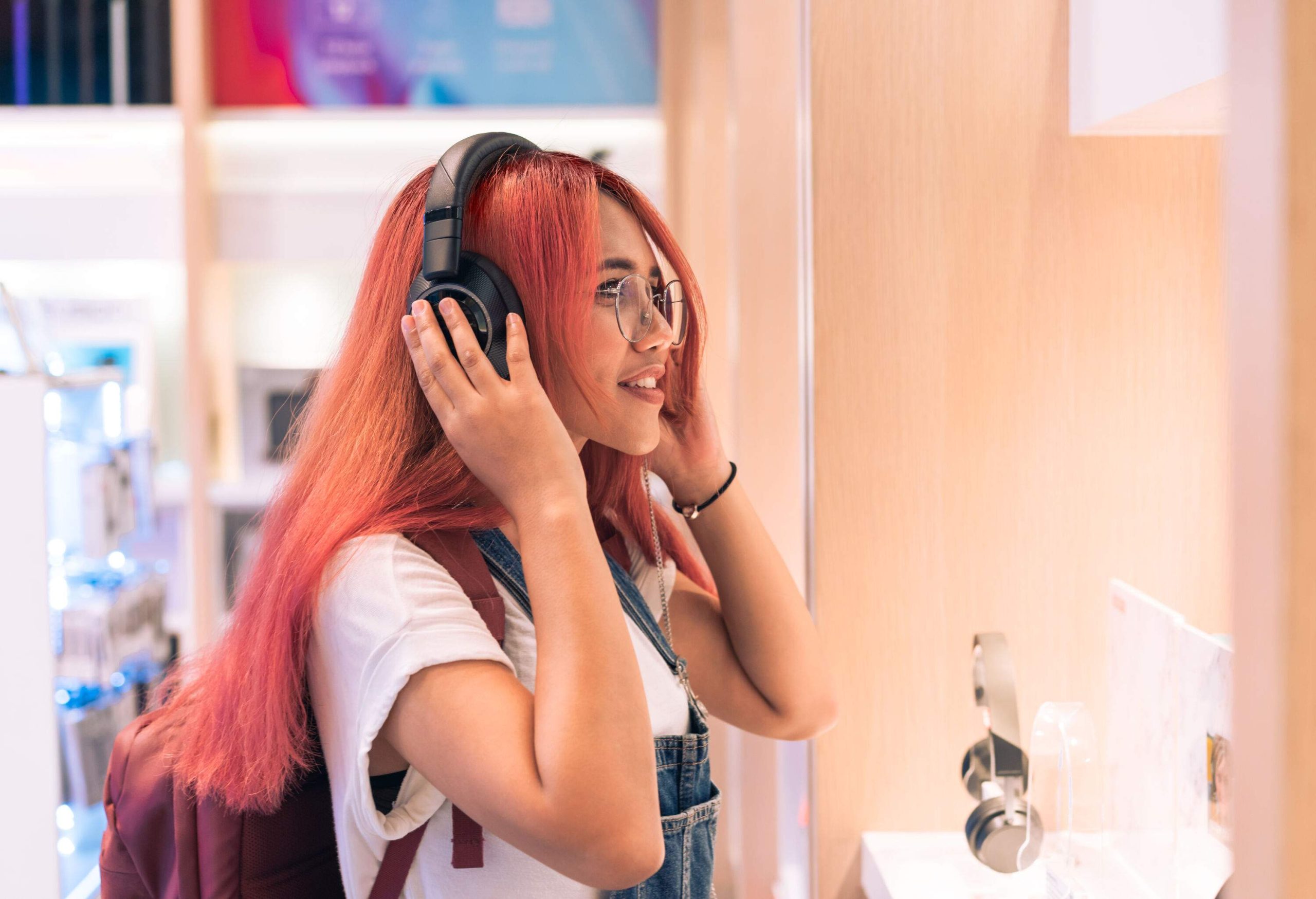 A happy female with long reddish hair trying on a headphone.