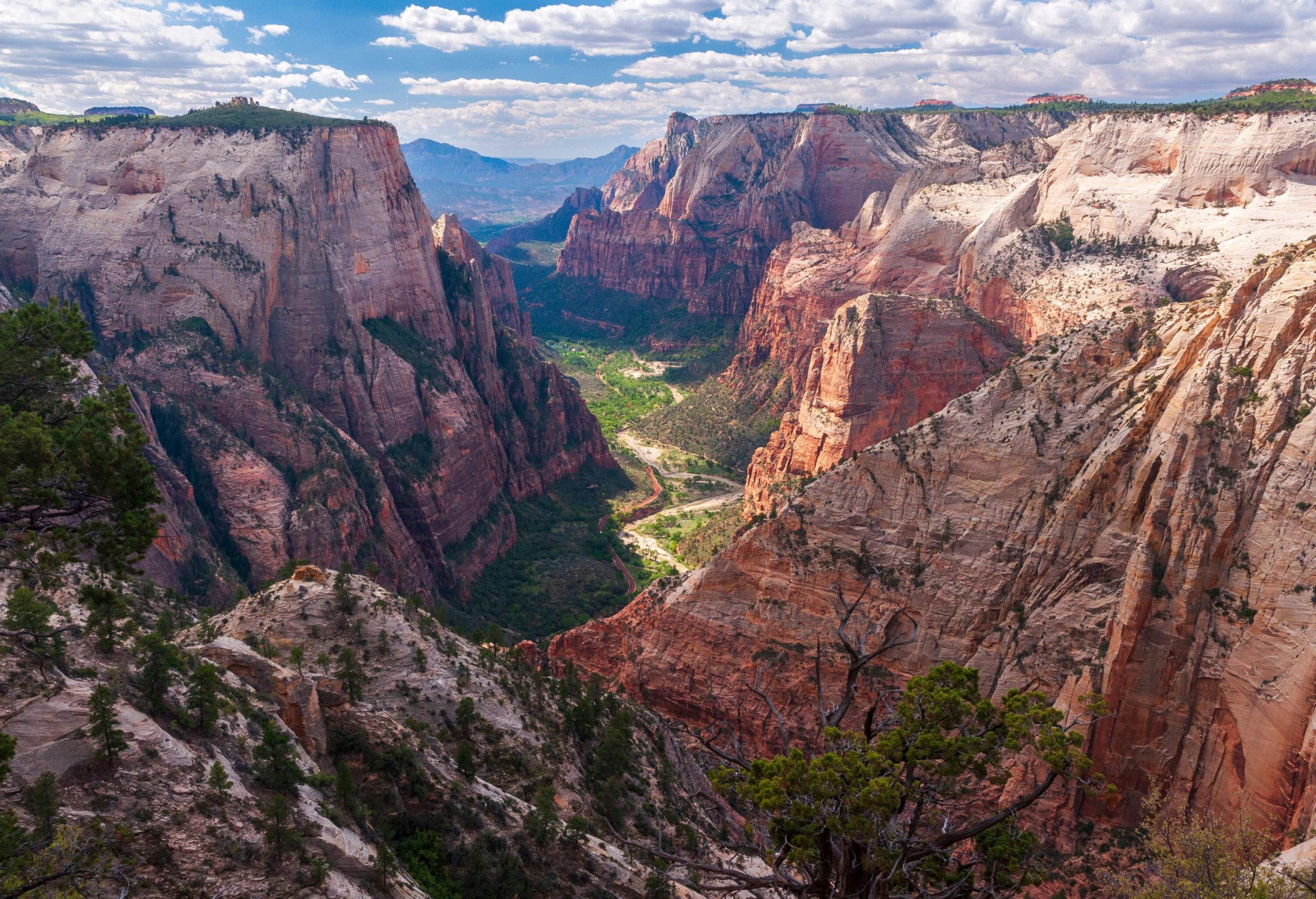 A stunning rocky mountain range dominates the horizon, with a picturesque valley nestled below, surrounded by steep cliffs.