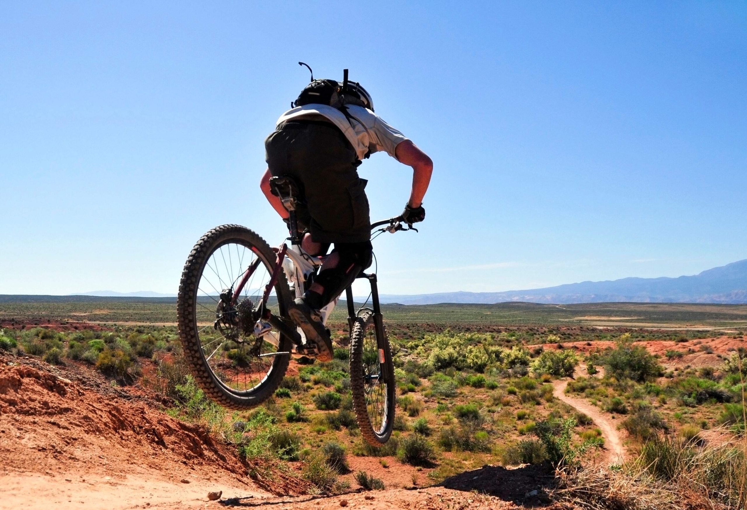 A man confidently rides his bike across a vast, barren, and grassy landscape, basking in the beauty of the clear blue sky above. 