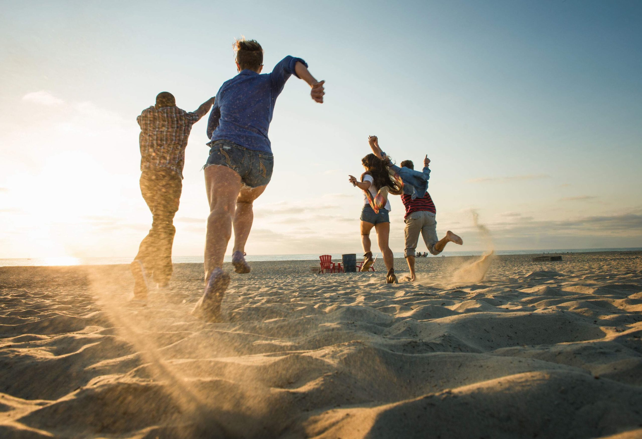 Four individuals run on the shore towards the sea.