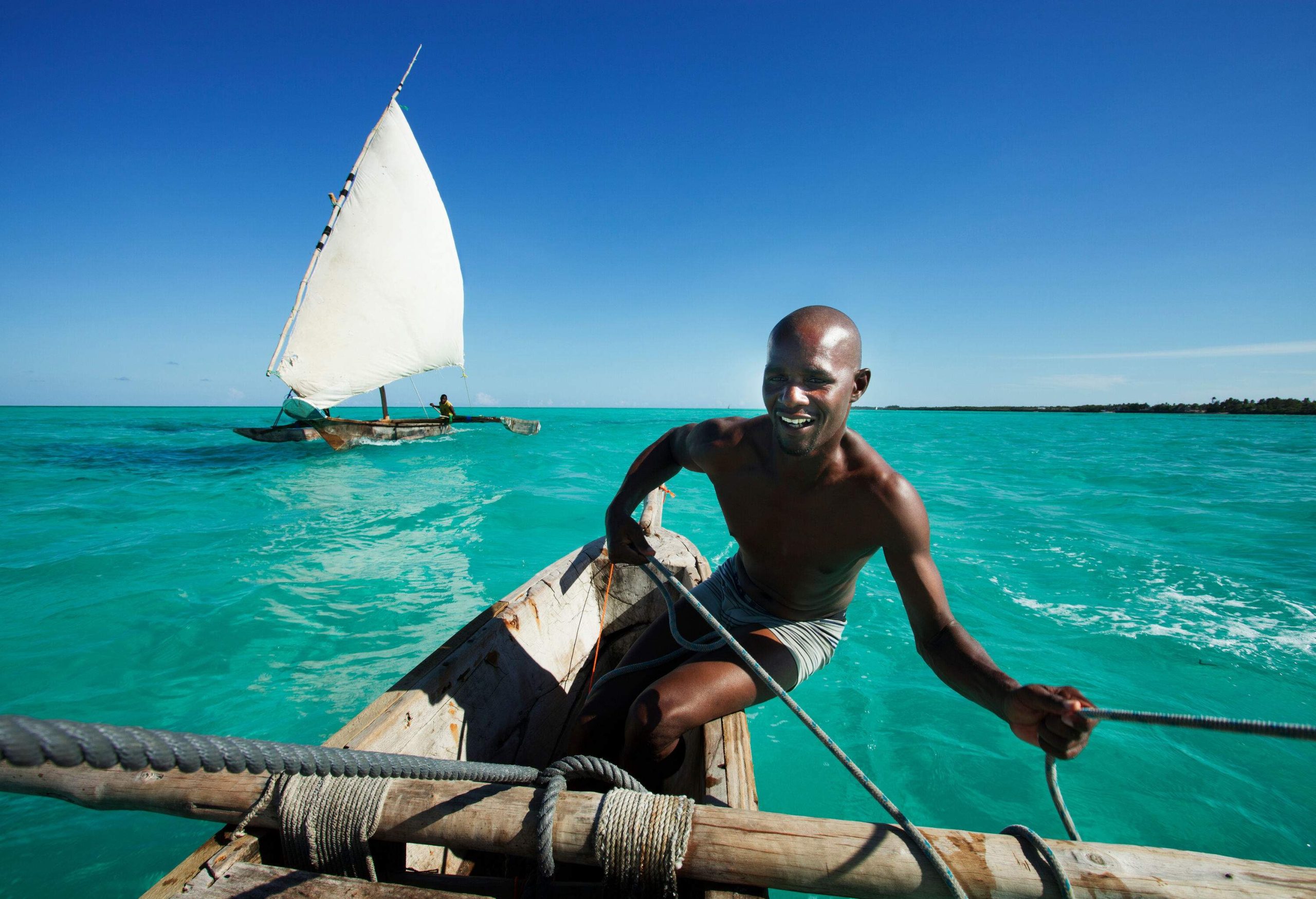 A topless man confidently steers a traditional sailing boat, his smile radiating the joy and freedom of navigating the open waters.