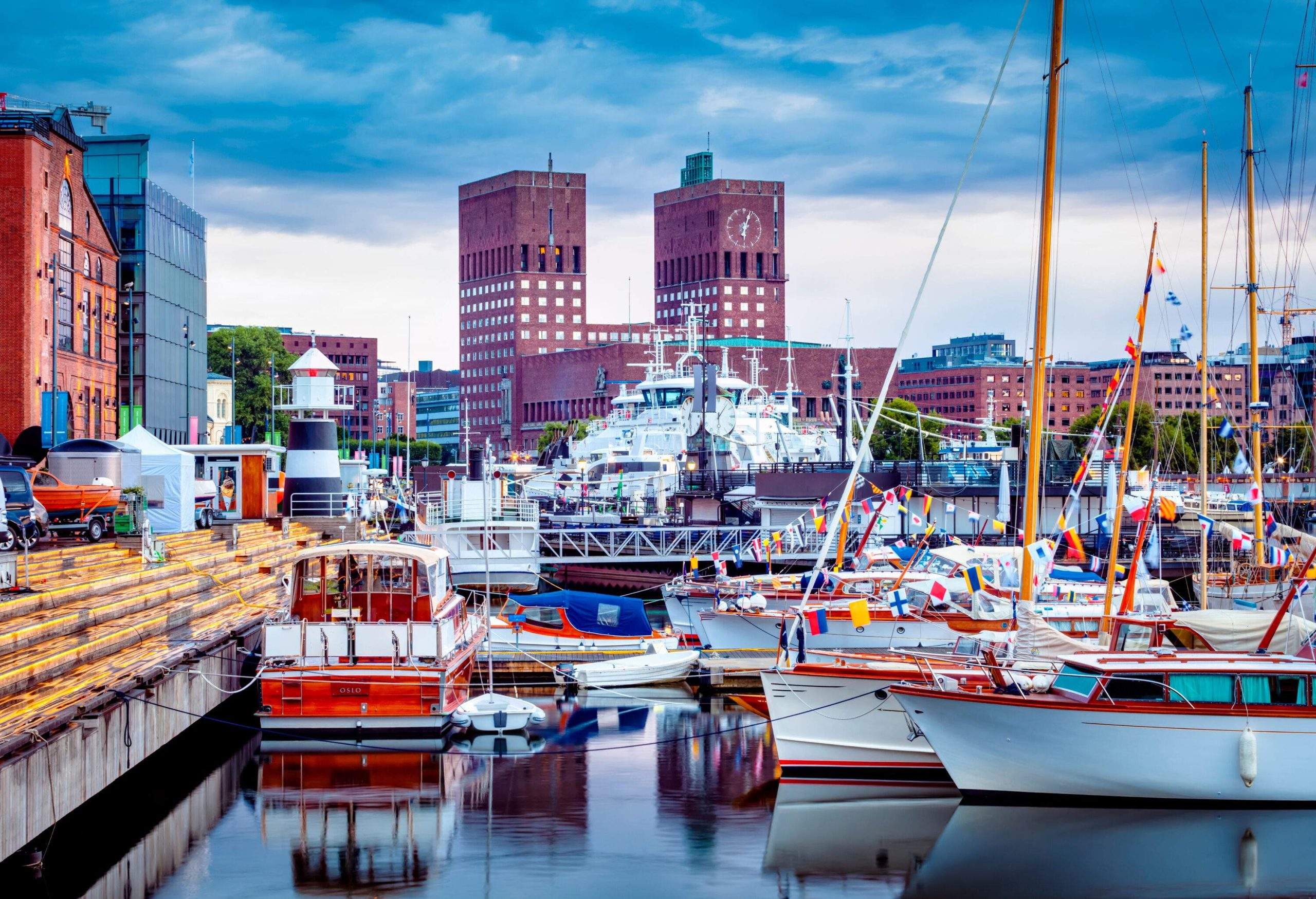 Docked boats with multicoloured flags affixed to their masts crowded into a harbour surrounded by stunning buildings.