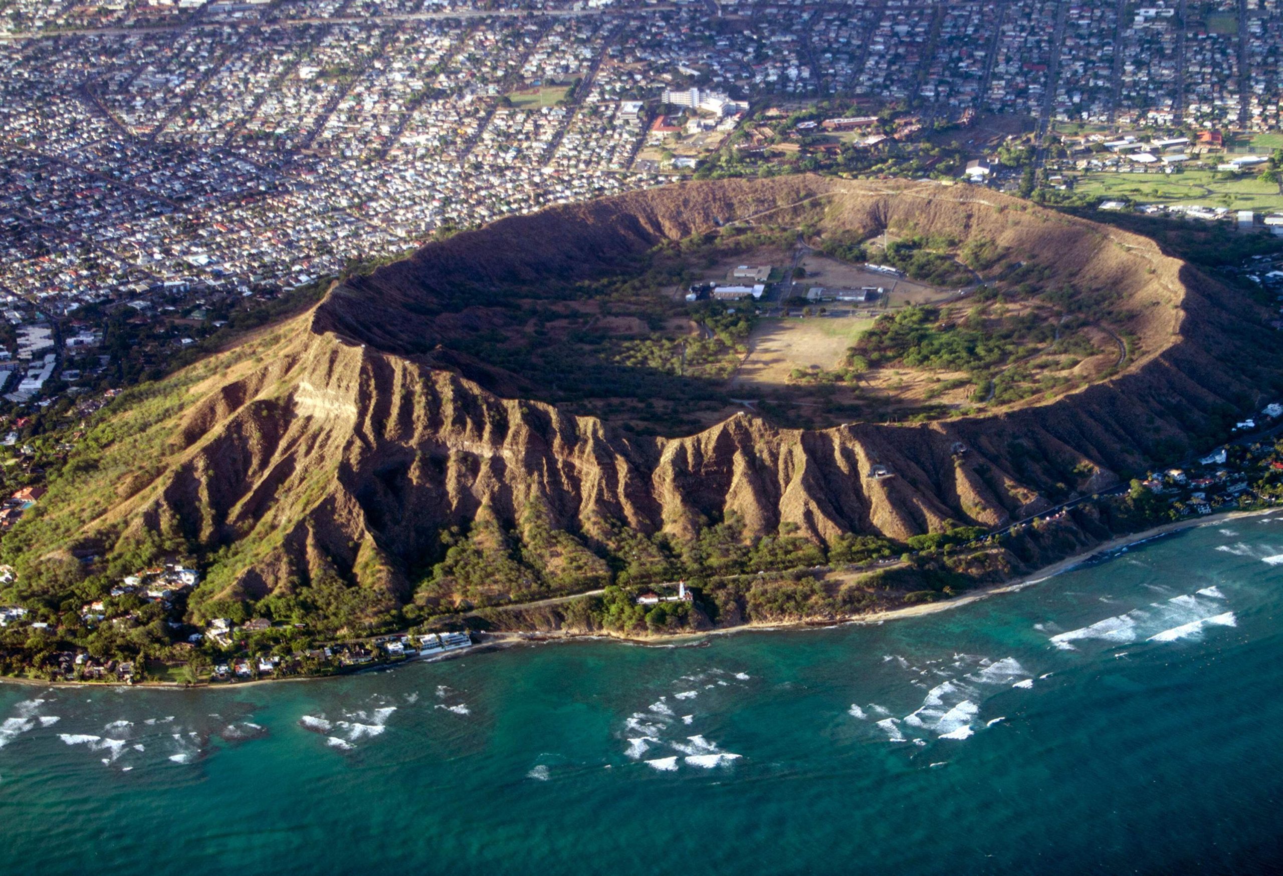 The iconic Diamond Head crater rises majestically, encircled by a bustling town located near the picturesque coast.