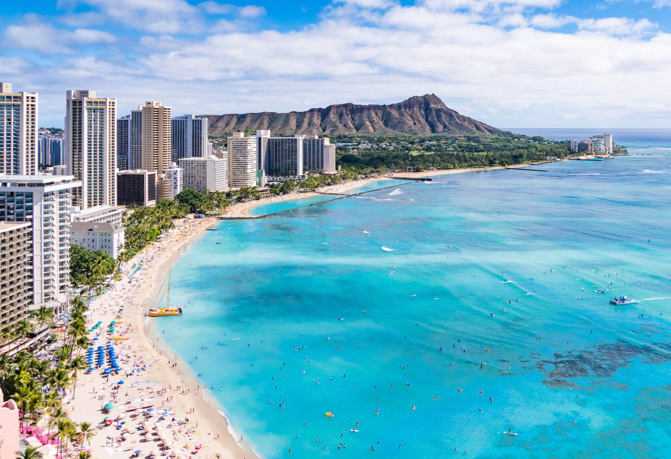 Waikiki Beach, adorned with hotels and buildings, stretches along the coastline, with the iconic Diamond Head Crater majestically rising in the distance.